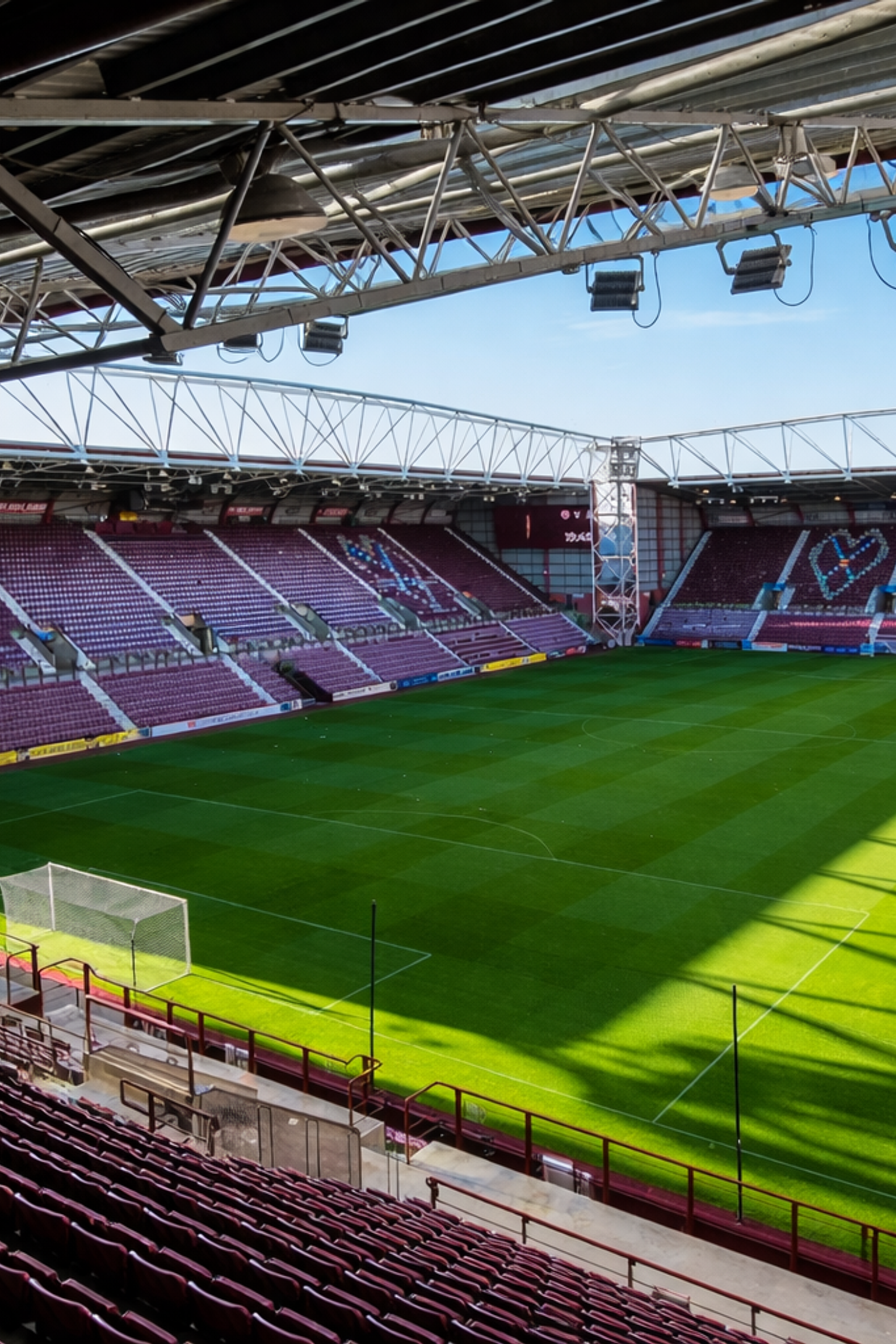 Leeg voetbalstadion met bordeauxrode stoelen die hartvormen vormen op de tribunes, en een groen veld.