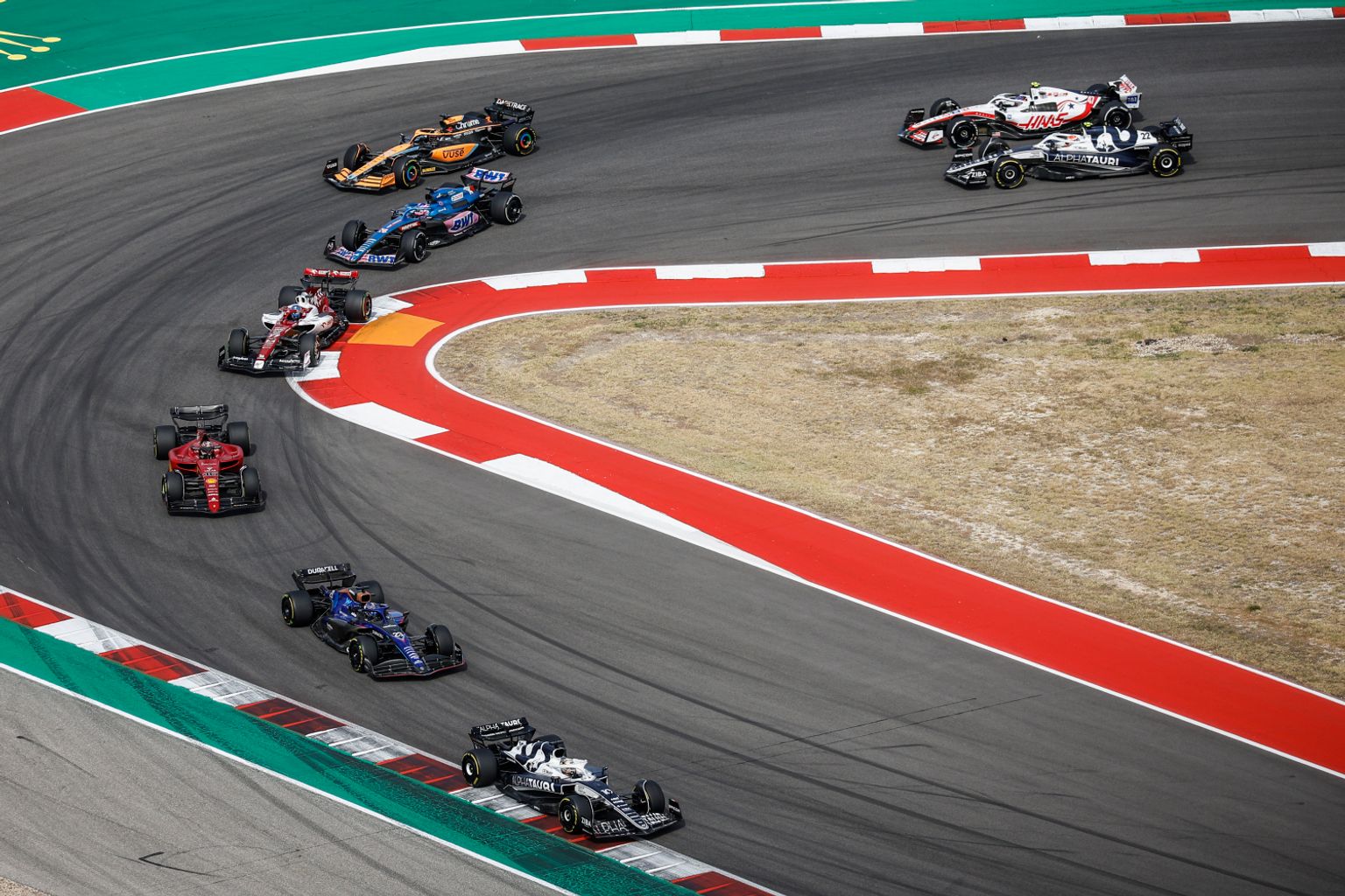 Flera Formel 1-bilar navigerar en bred kurva på en racerbana.