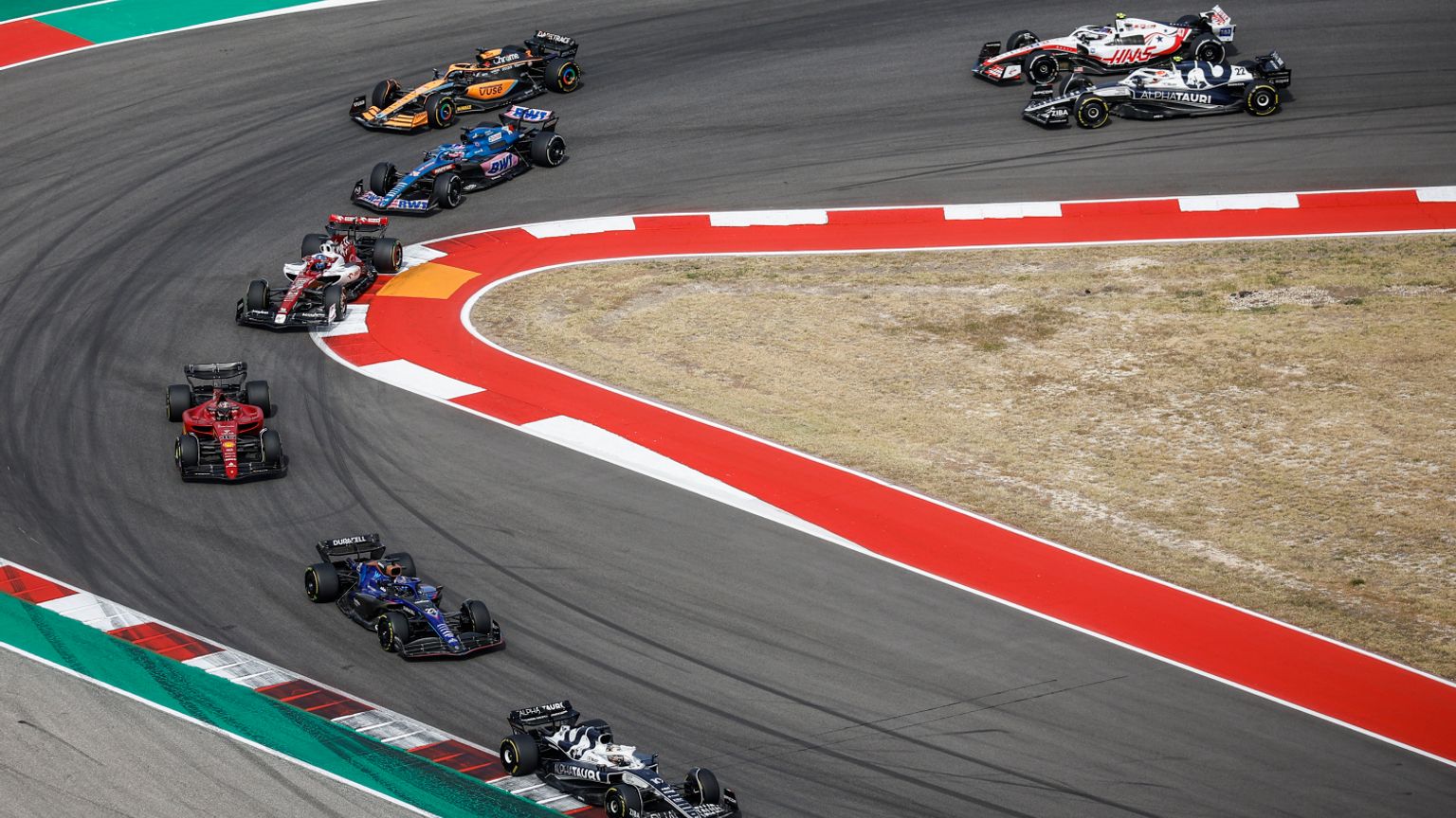 Flera Formel 1-bilar navigerar en bred kurva på en racerbana.