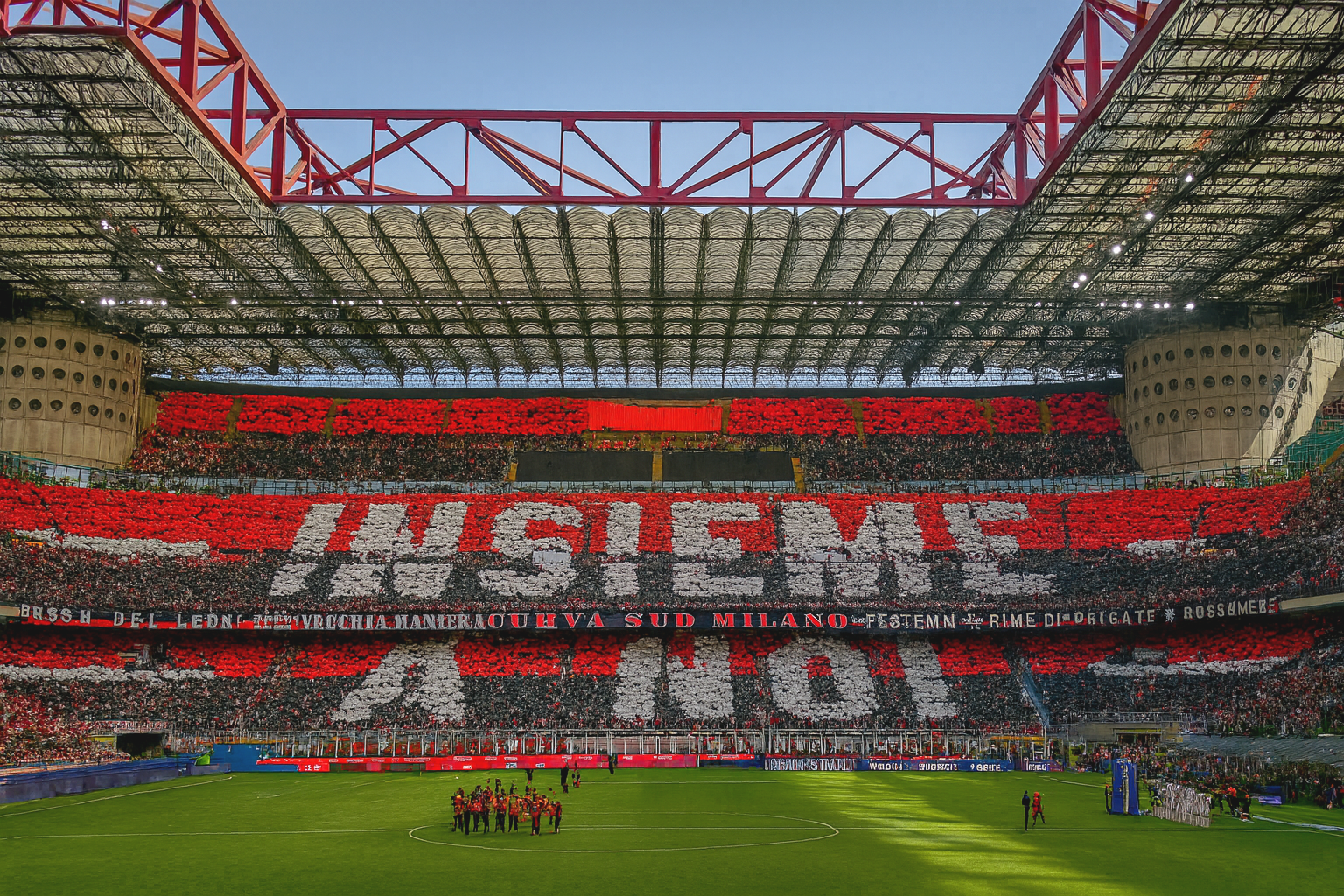 Ein Stadion gefüllt mit Fans, die rote, schwarze und weiße Karten halten, um "INSIEME" und andere Nachrichten zu buchstabieren, mit einer Fußballmannschaft auf dem grünen Spielfeld.