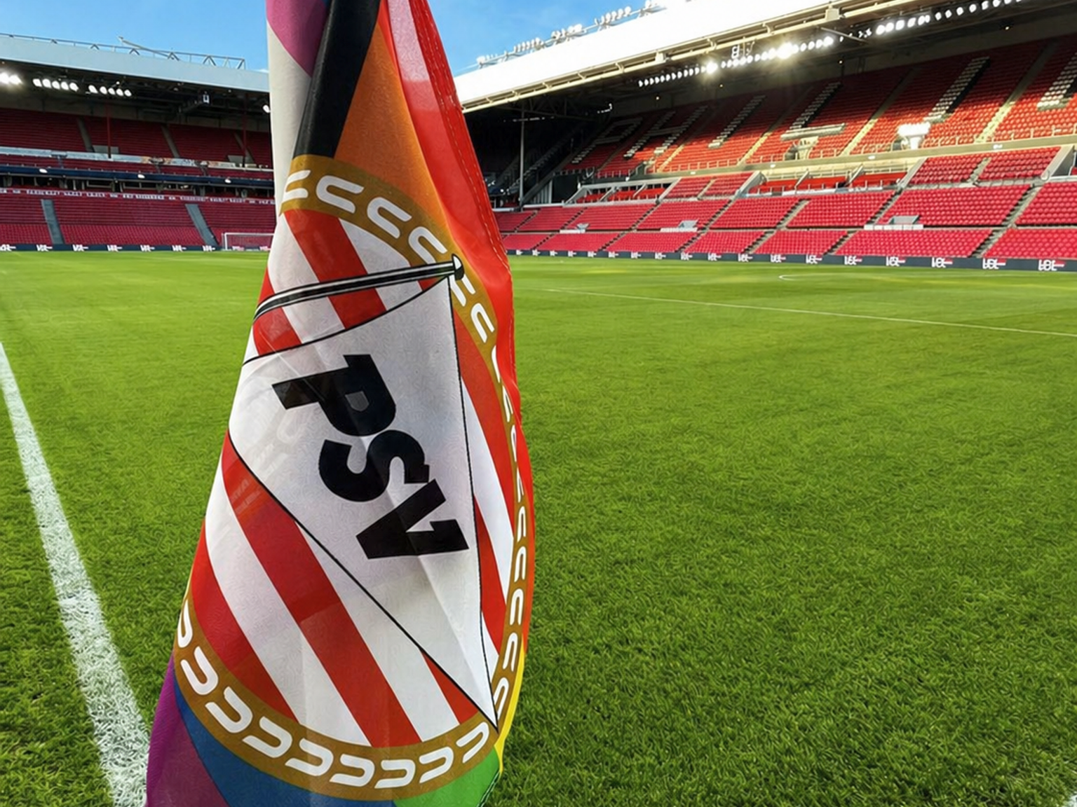 Zwei große Fahnen, eine mit PSV-Branding und eine andere mit einem Bulldoggen-Design, wehen über einer Stadionmenge mit erhobenen Fäusten.