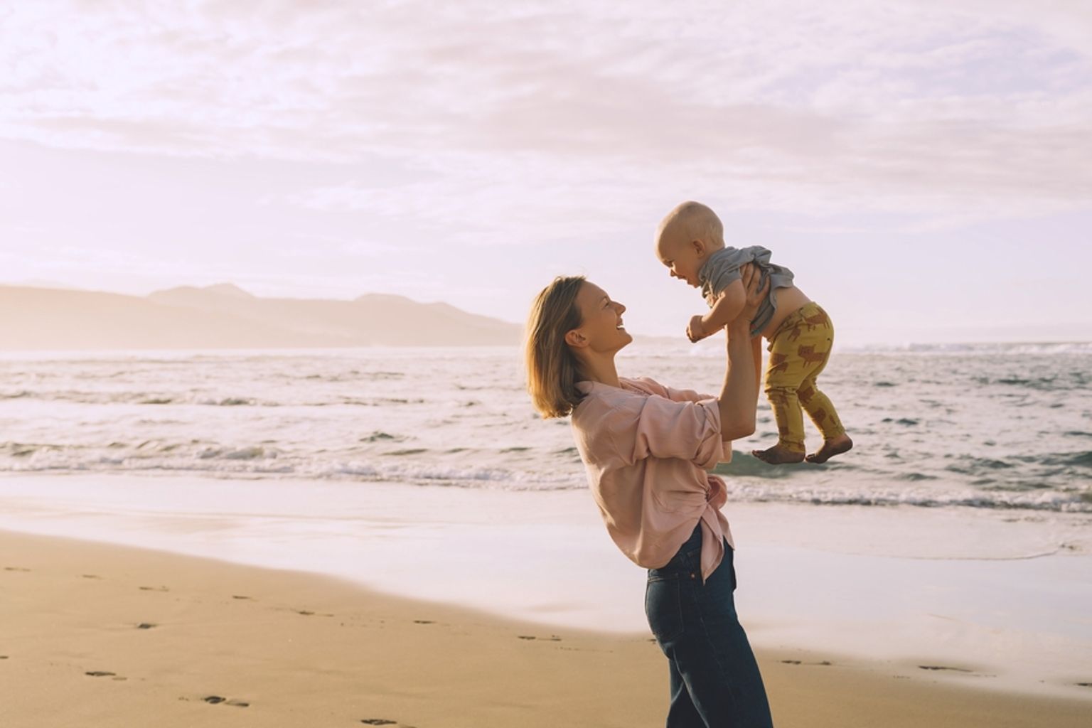 en kvinna hÄller en bebis i sina armar pÄ stranden.