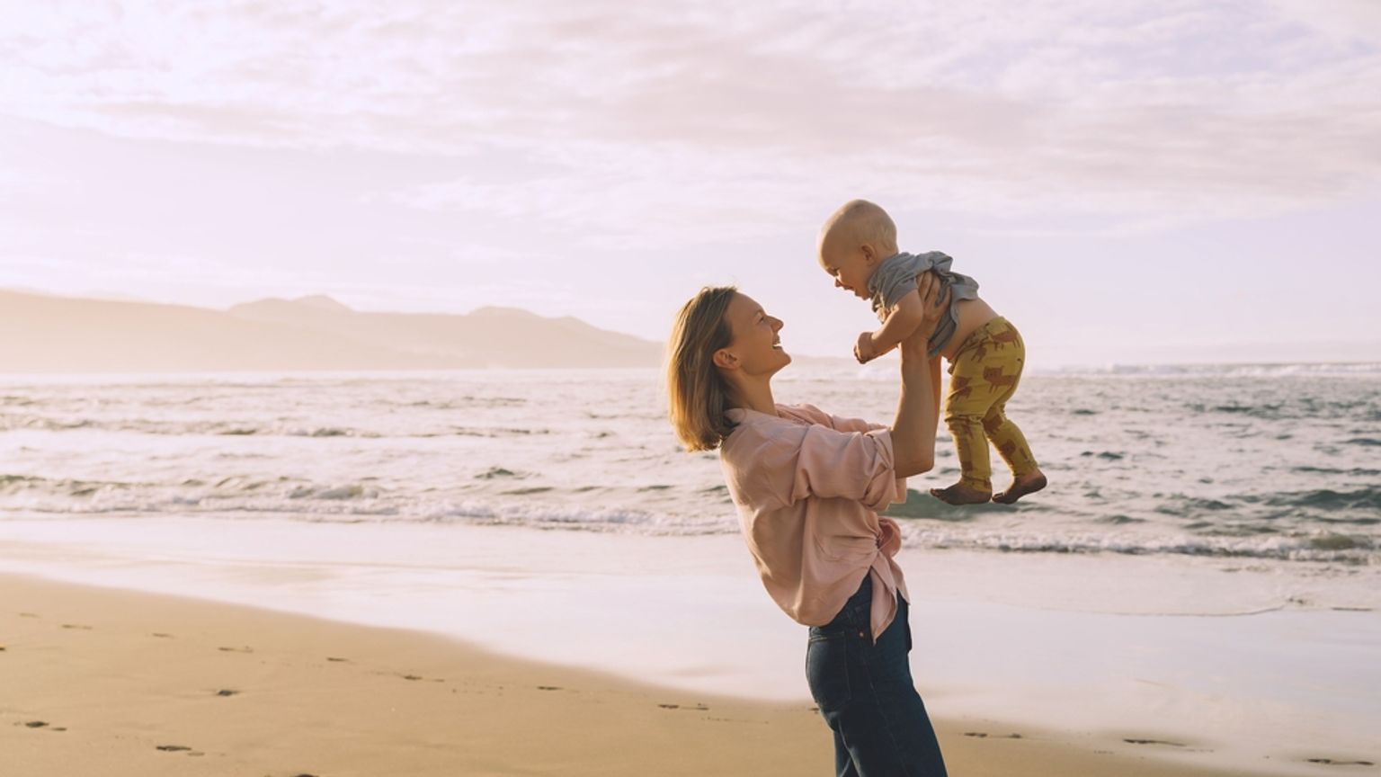 en kvinna hÄller en bebis i sina armar pÄ stranden.