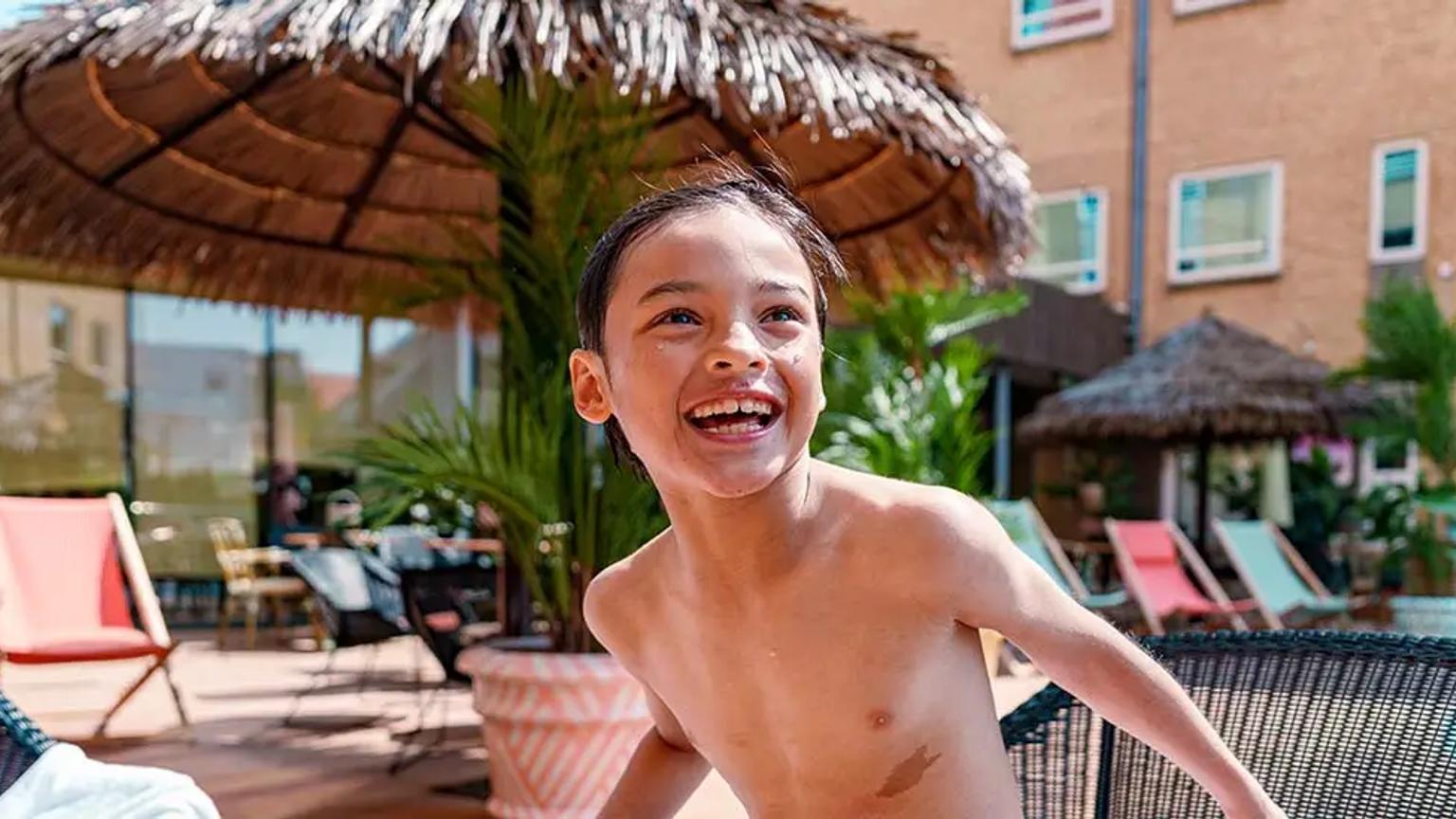 en skjortlös ung pojke står bredvid en swimmingpool.