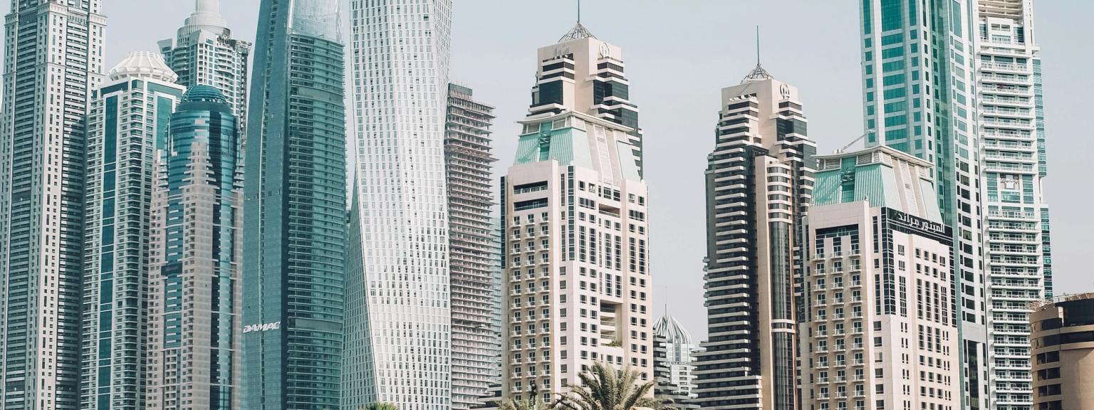 een groep mensen die op kamelen rijden op een strand voor een stadsgezicht