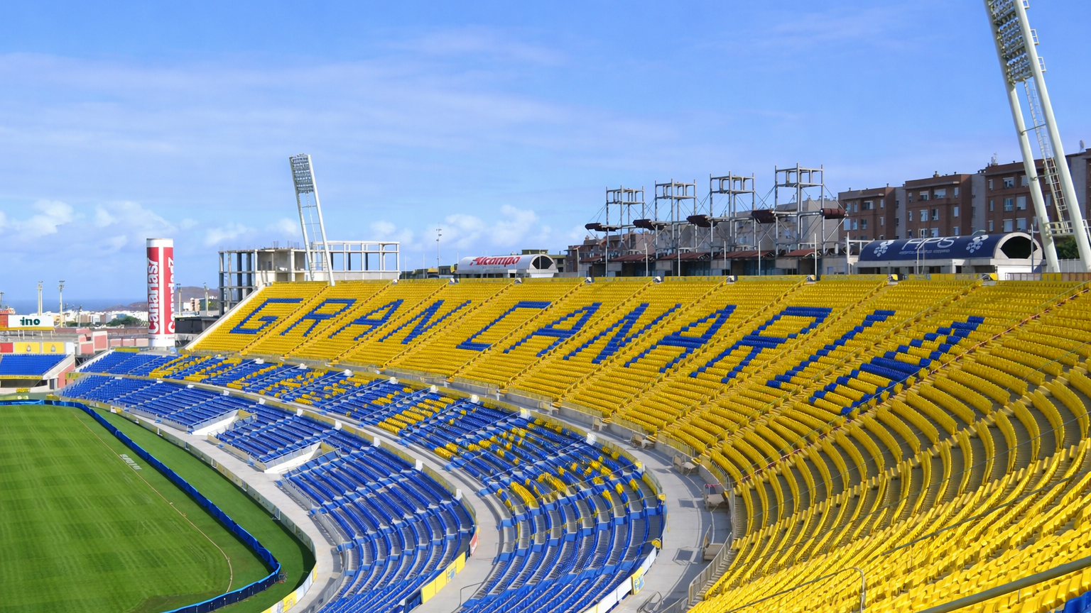 Empty stadium with yellow and blue seats spelling out "GRAN CANARIA" under a blue sky.