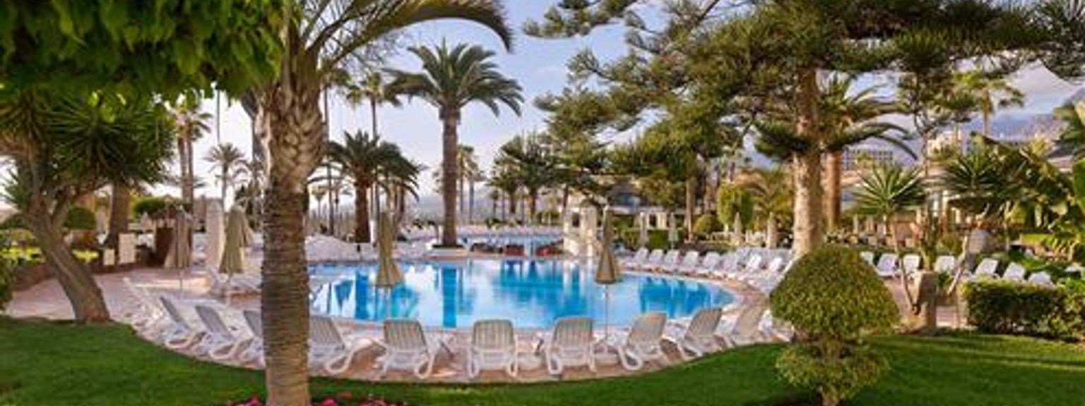 en stor swimmingpool omgiven av palmer och stolar i en frodig grön park.