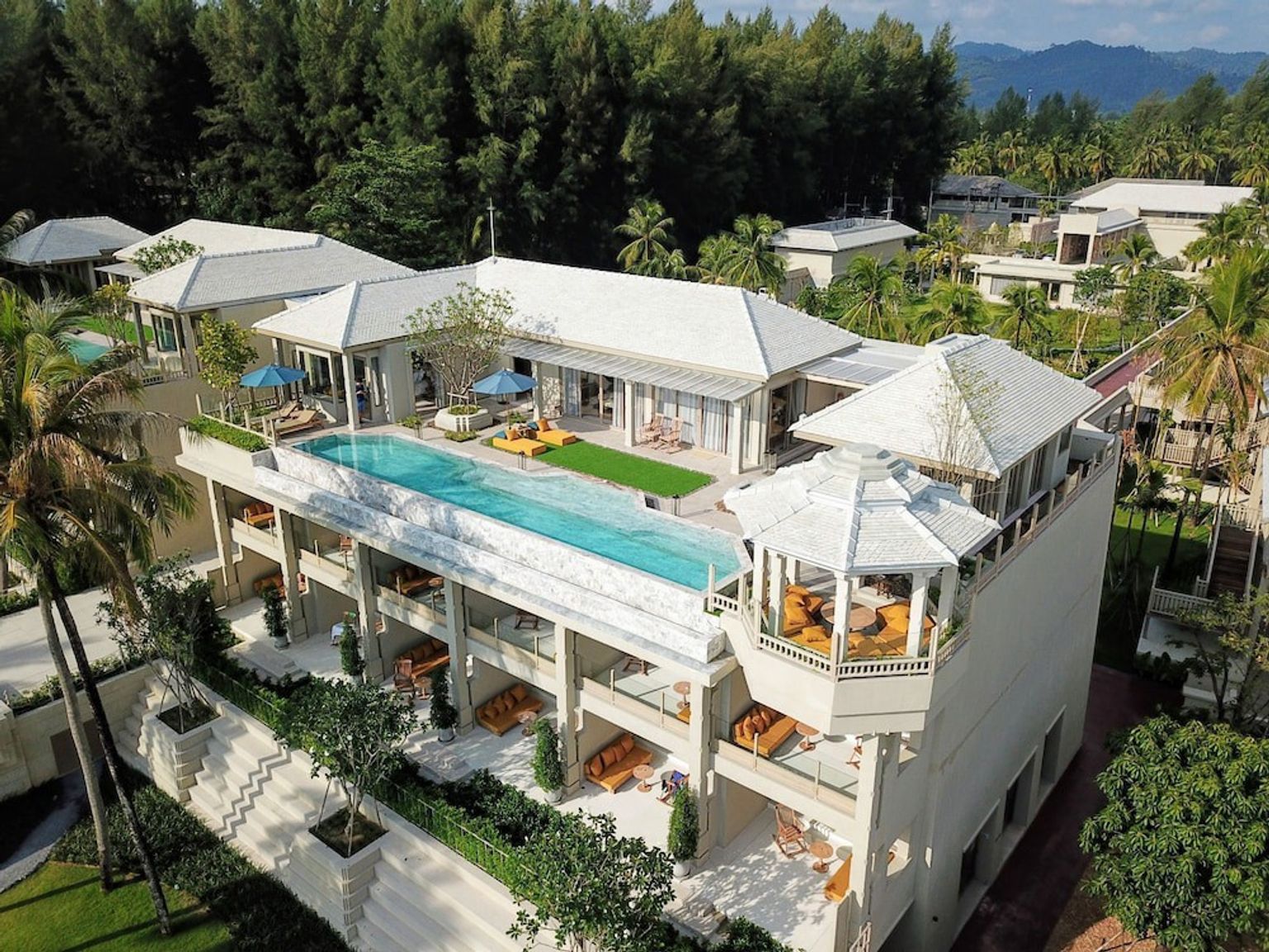 an aerial view of a large white house with a swimming pool on the roof surrounded by palm trees.