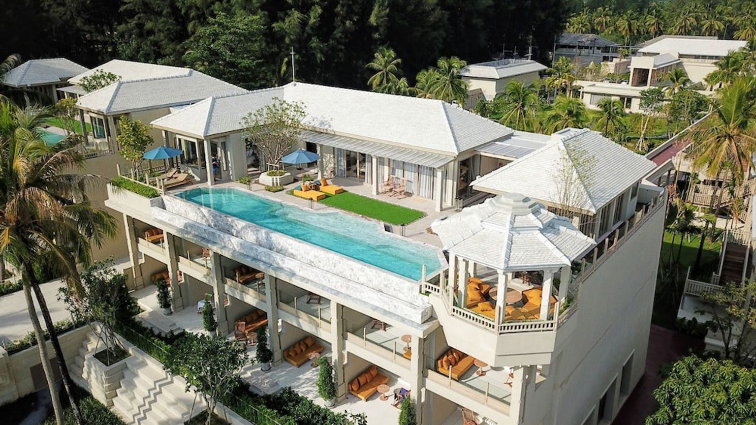 en flygvy av ett stort vitt hus med en swimmingpool på taket omgivet av palmer.