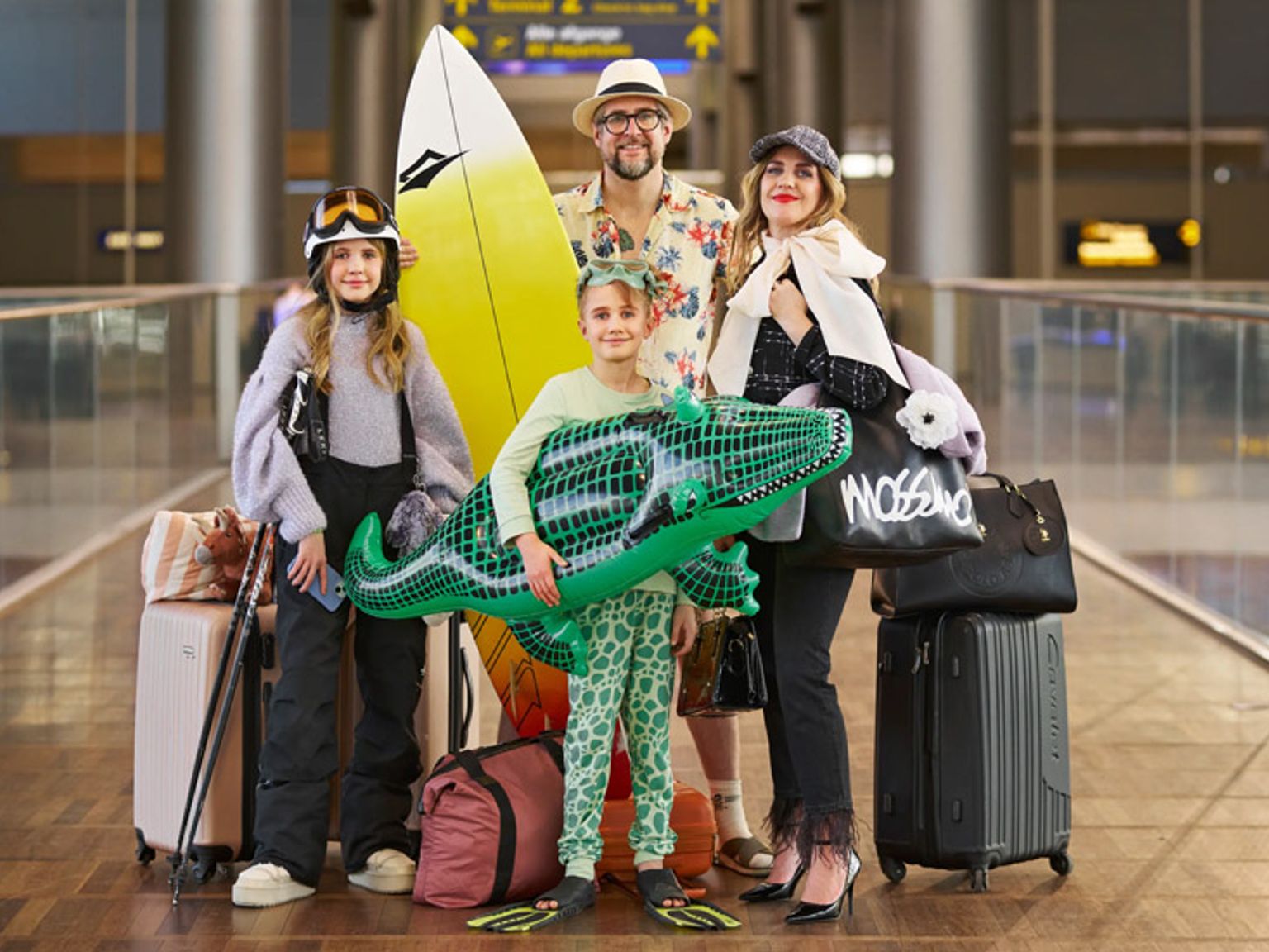 en familie står i en lufthavn med bagage og et surfbræt