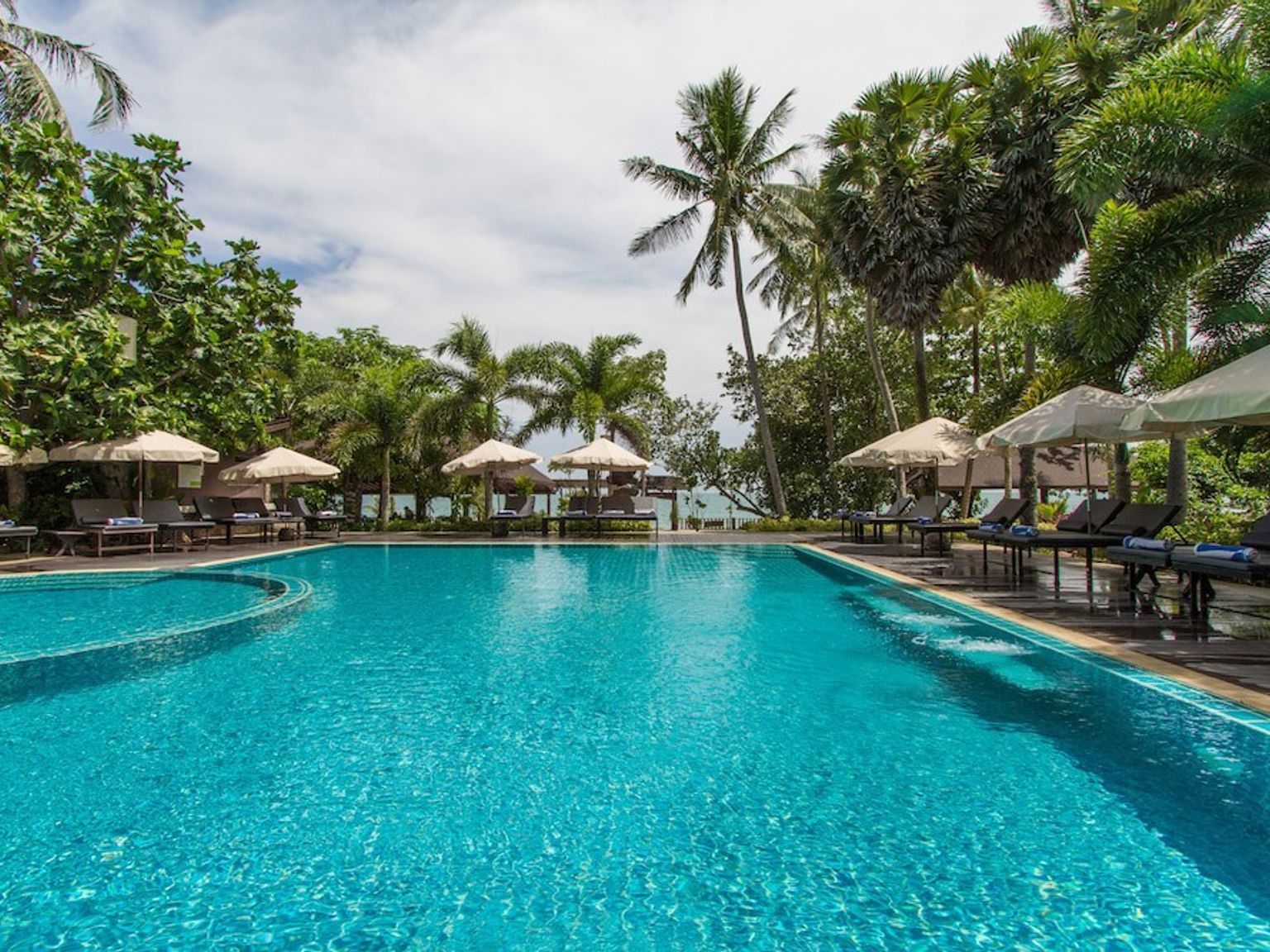 duży basen otoczony krzesłami i parasolami w ośrodku