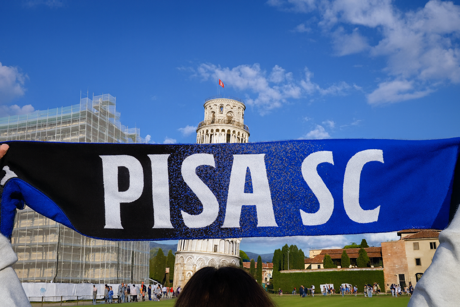 A fan holds a blue and black "PISA SC" scarf in front of the Leaning Tower of Pisa.