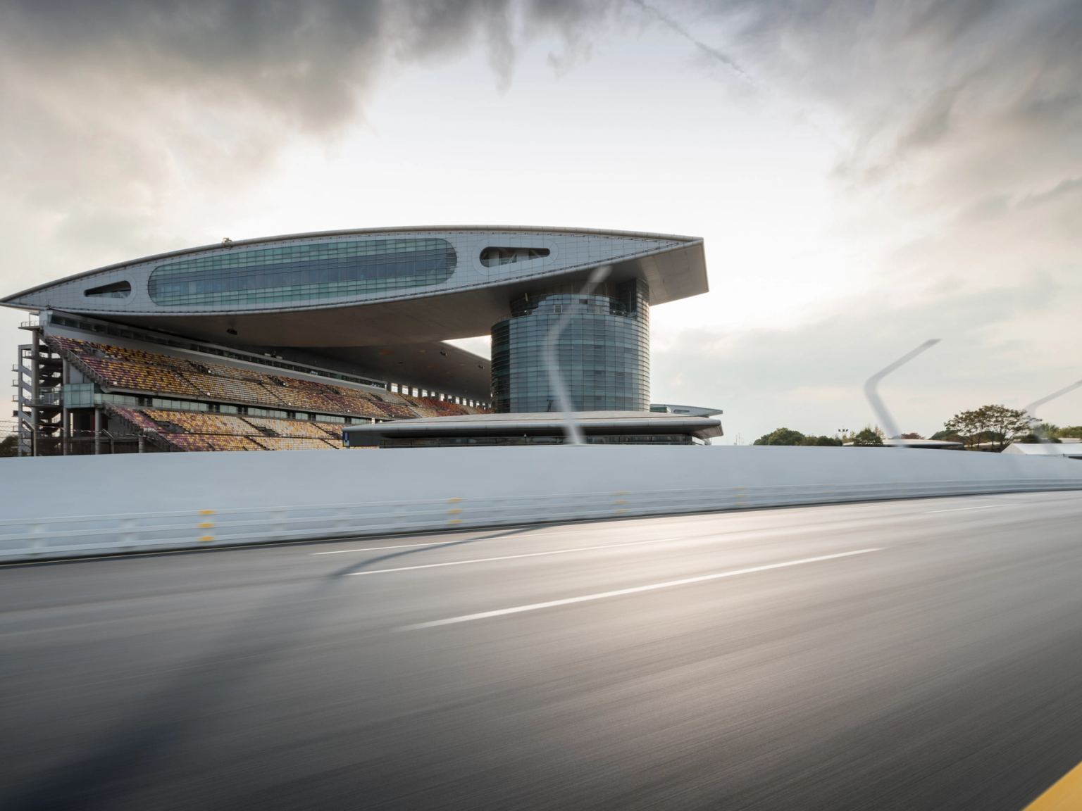 Modern race track grandstand with a curved roof and seating, viewed from a blurred track.