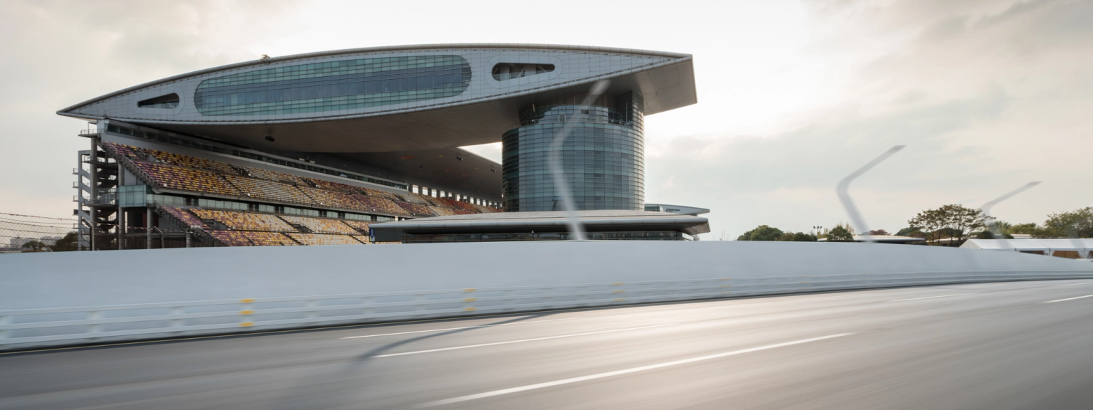 Modern race track grandstand with a curved roof and seating, viewed from a blurred track.