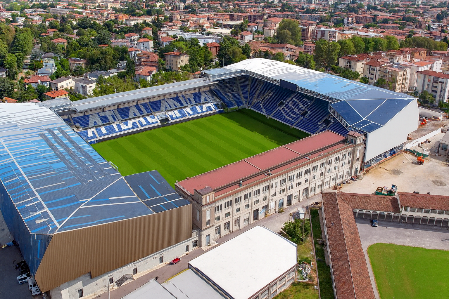 Aerial view of a modern stadium with a green pitch and blue seats spelling "ATALANTA," surrounded by an urban landscape.