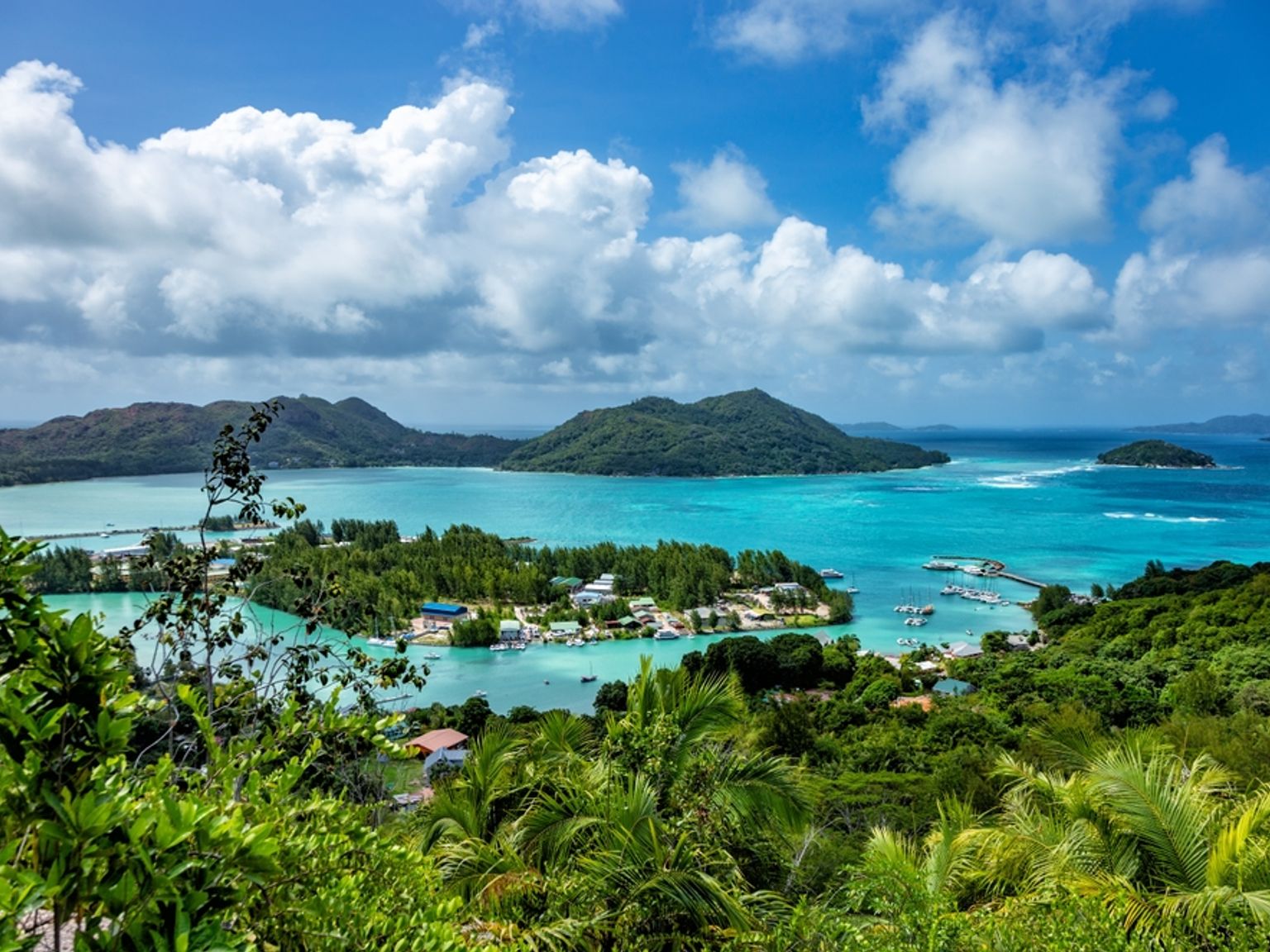 Panoramisk udsigt over en tropisk bugt med turkis vand, frodige grønne øer og en kystby. Seychellerne