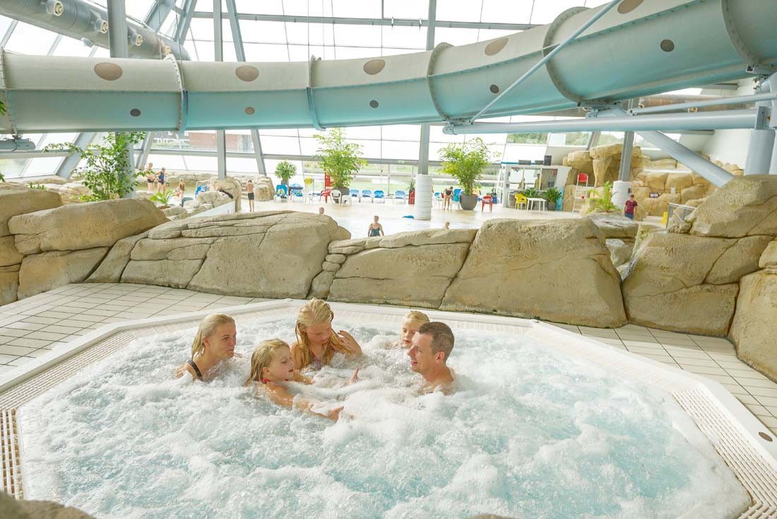 En familj på fem njuter av en bubblande bubbelpool på ett modernt inomhusvattenland.