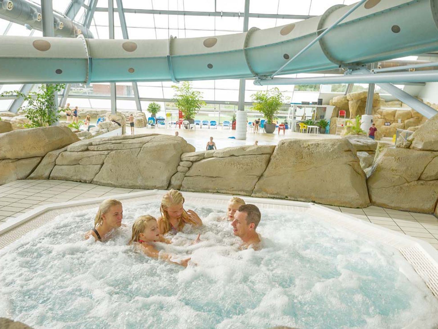 En familj på fem njuter av en bubblande bubbelpool på ett modernt inomhusvattenland.