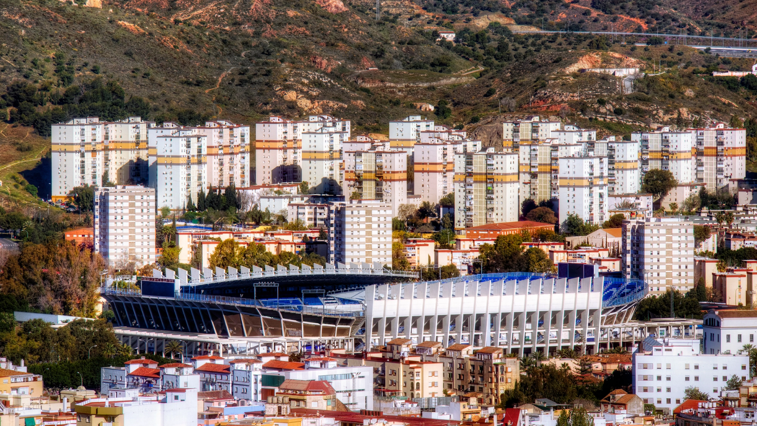 Una ciudad con un gran estadio, numerosos edificios residenciales y colinas al fondo.