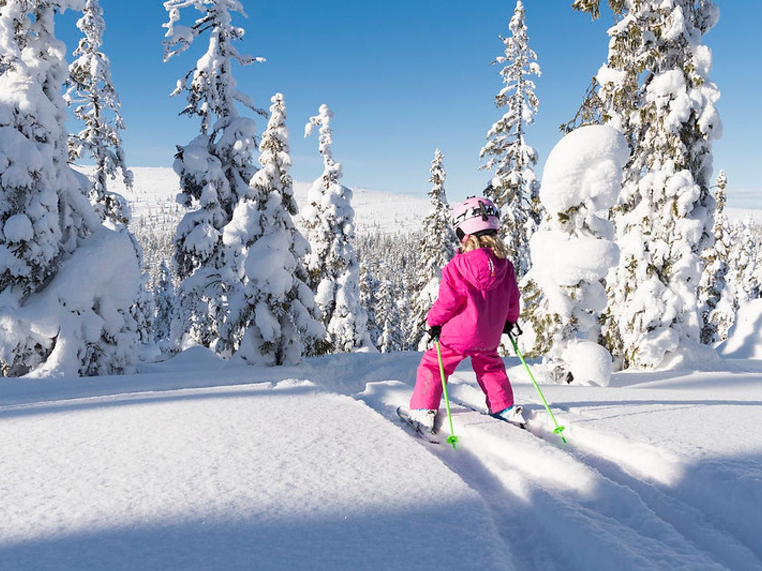 en liten jente står på ski ned en snødekt bakke.