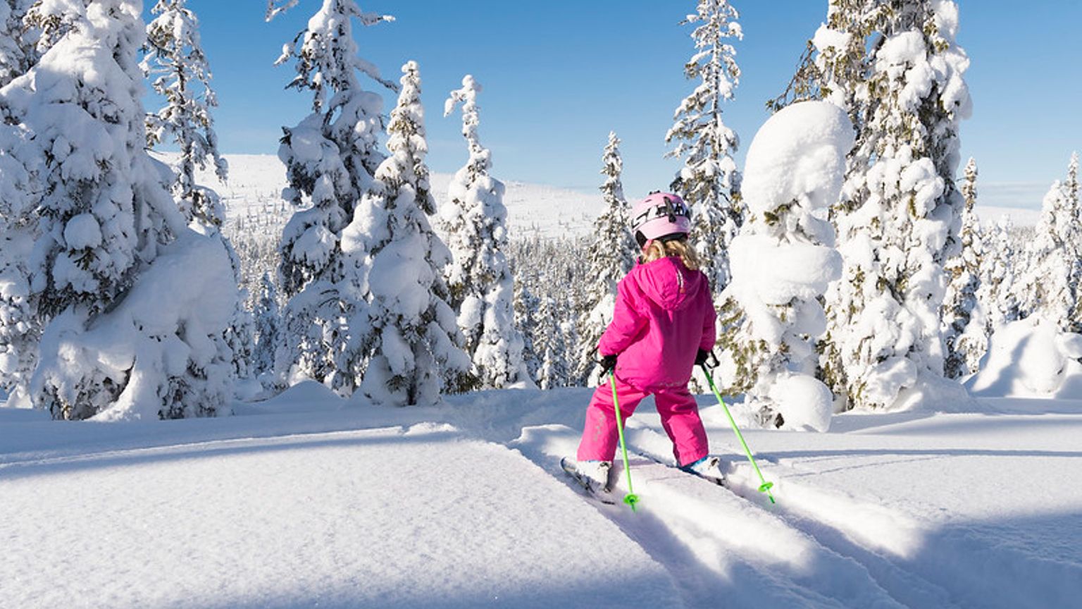 en lille pige står på ski ned ad en sneklædt bakke.