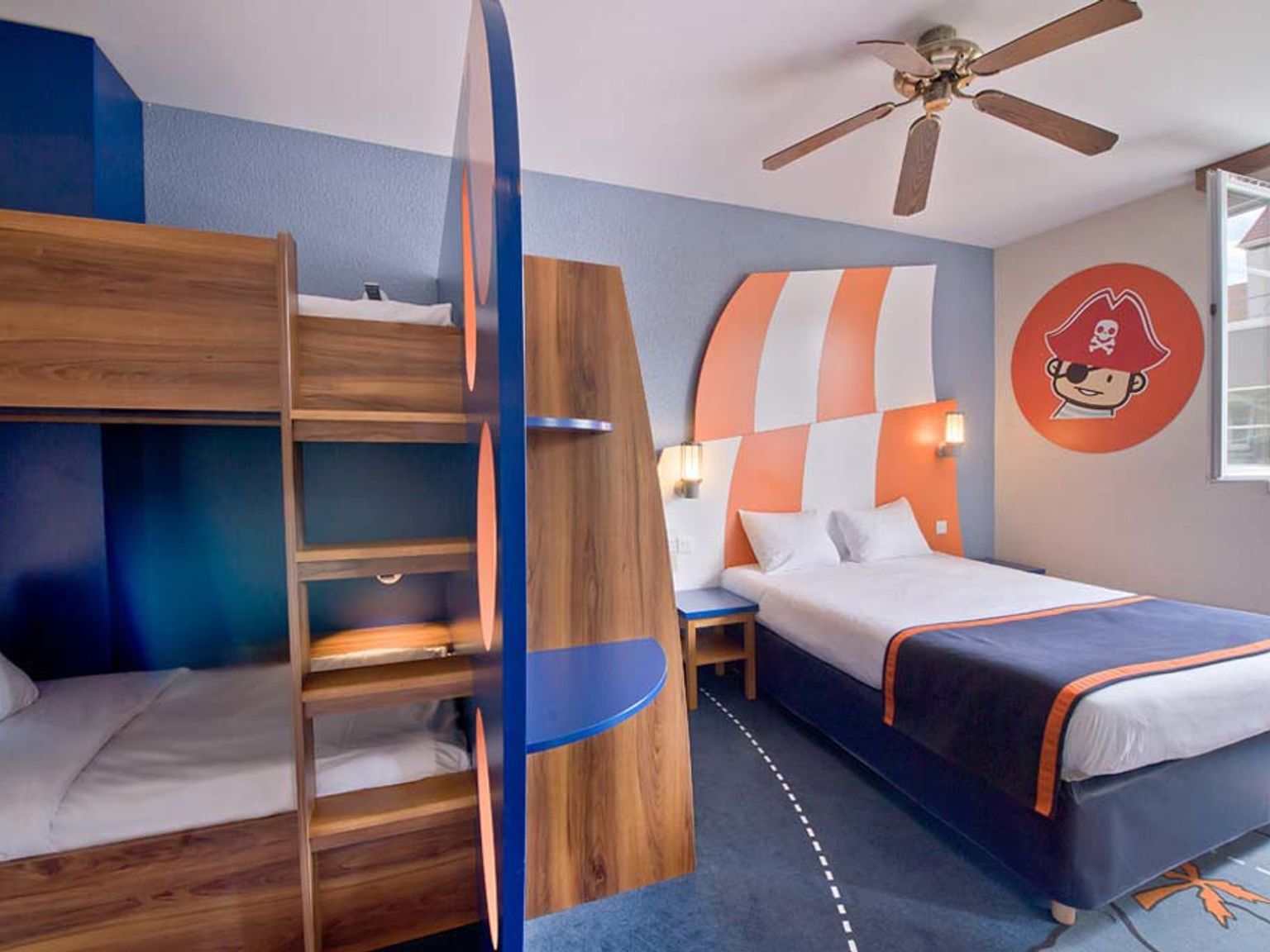 Ett sovrum med pirattema med en dubbelsäng, våningssängar och en tecknad piratdekal på väggen. Explorers Hotel på Disneyland® Paris