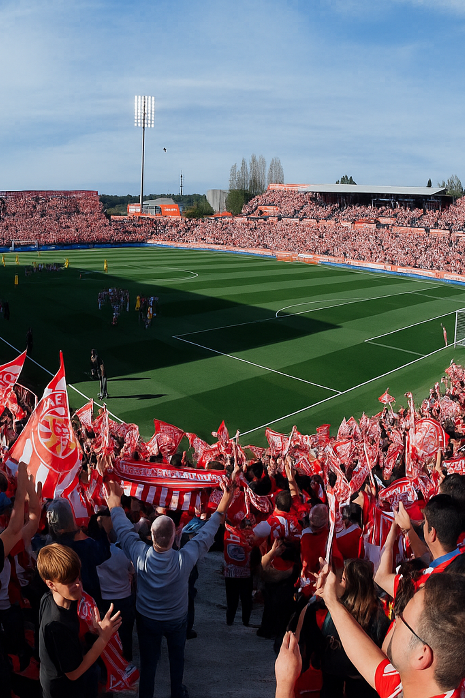 Pełny stadion piłkarski z kibicami machającymi czerwono-białymi flagami Girony.