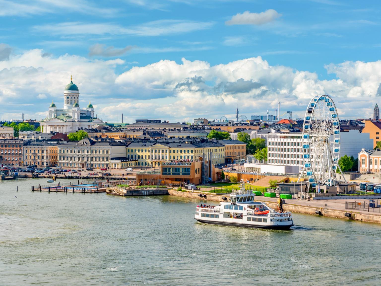 Helsingfors bysilhuett med en hvit katedral, et pariserhjul og en ferge på vannet under en blå himmel.