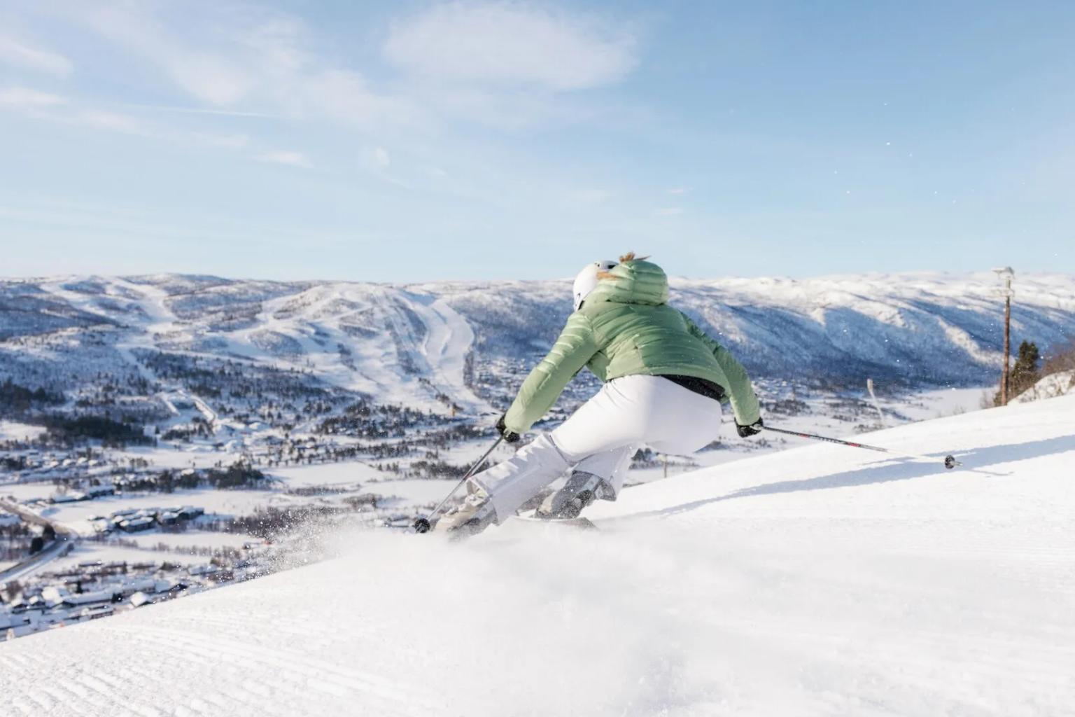 en kvinne står på ski ned en snødekt bakke.