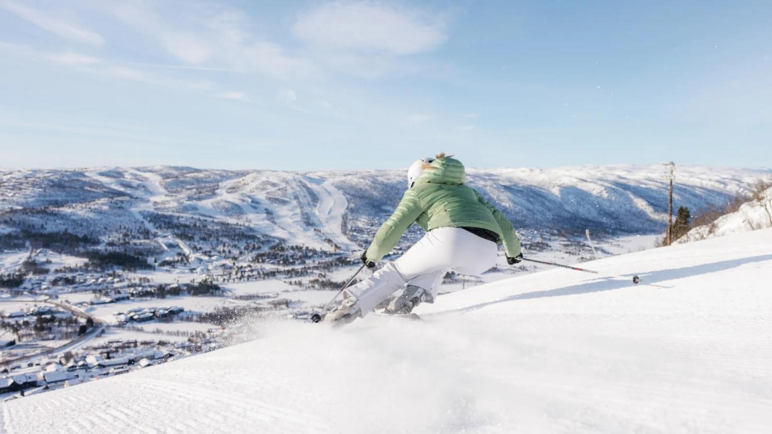 en kvinne står på ski ned en snødekt bakke.