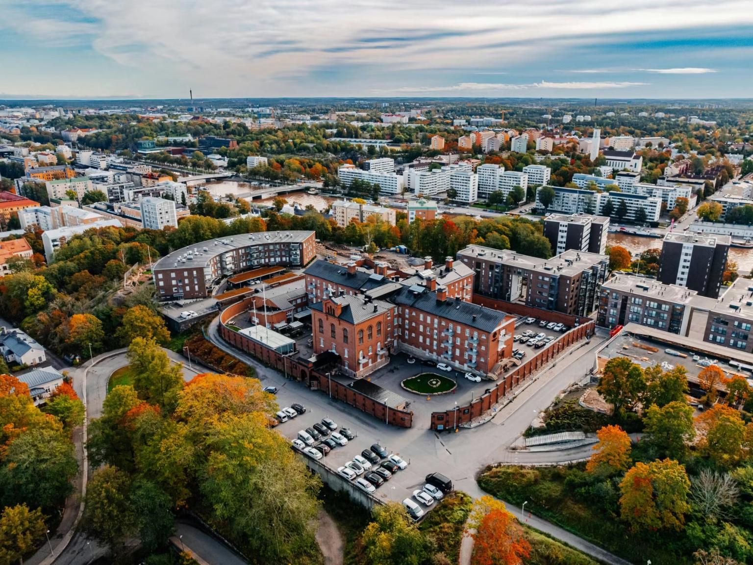 Luftfoto af en by om efteråret, der viser et gammelt murstensbygningskompleks, moderne lejligheder og en flod.