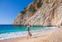 Een kind doet een handstand op een zandstrand met turquoise water en een grote rotsachtige klif. Antalya - Turkije