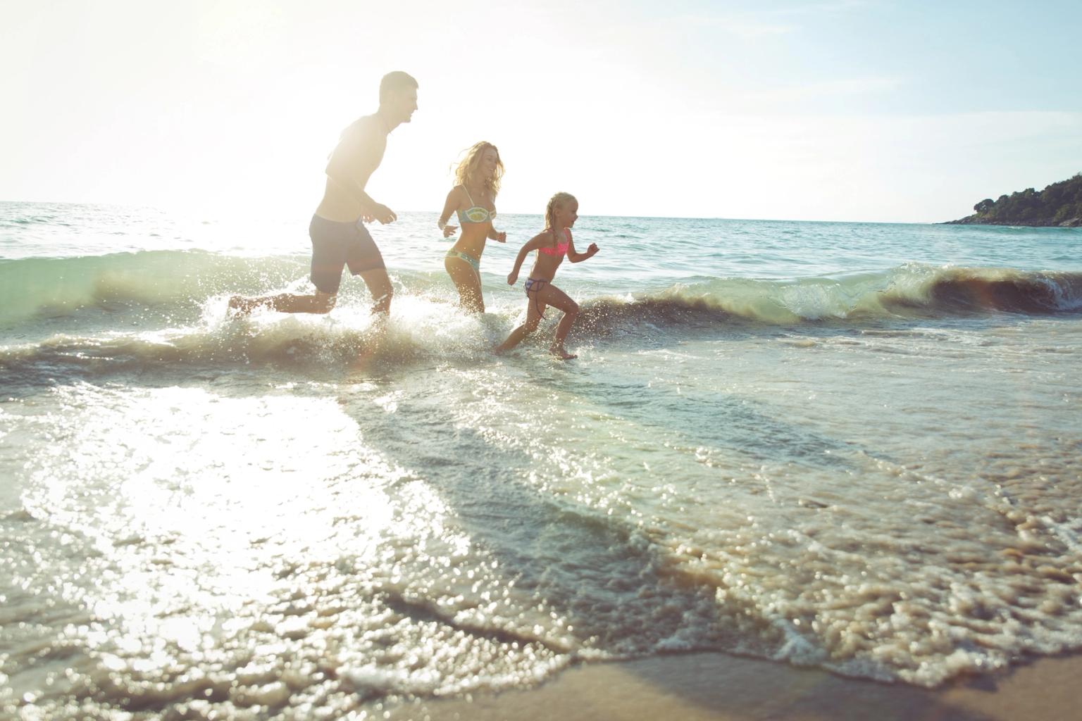 Familj springer i havsvågorna på en solig strand i Thailand
