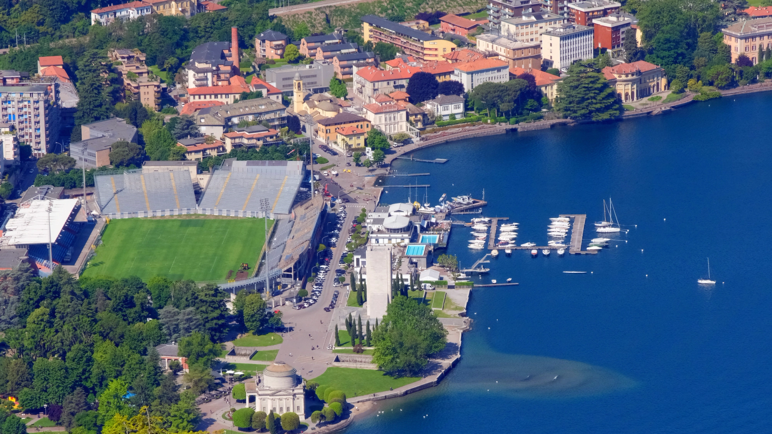 Luftaufnahme einer Stadt am See mit einem Stadion und einem Yachthafen voller Boote.