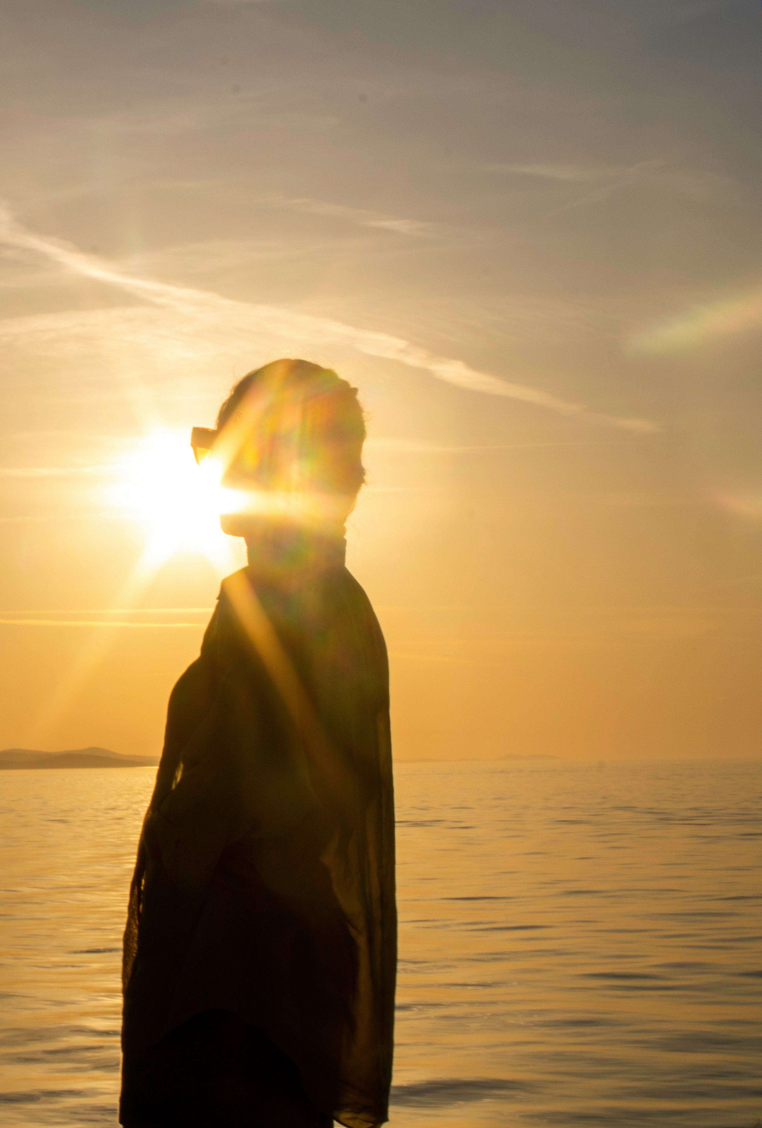 Silhuet af en person med den klare nedgående sol bag deres hoved over havet, hvilket skaber en linseeffekt.
