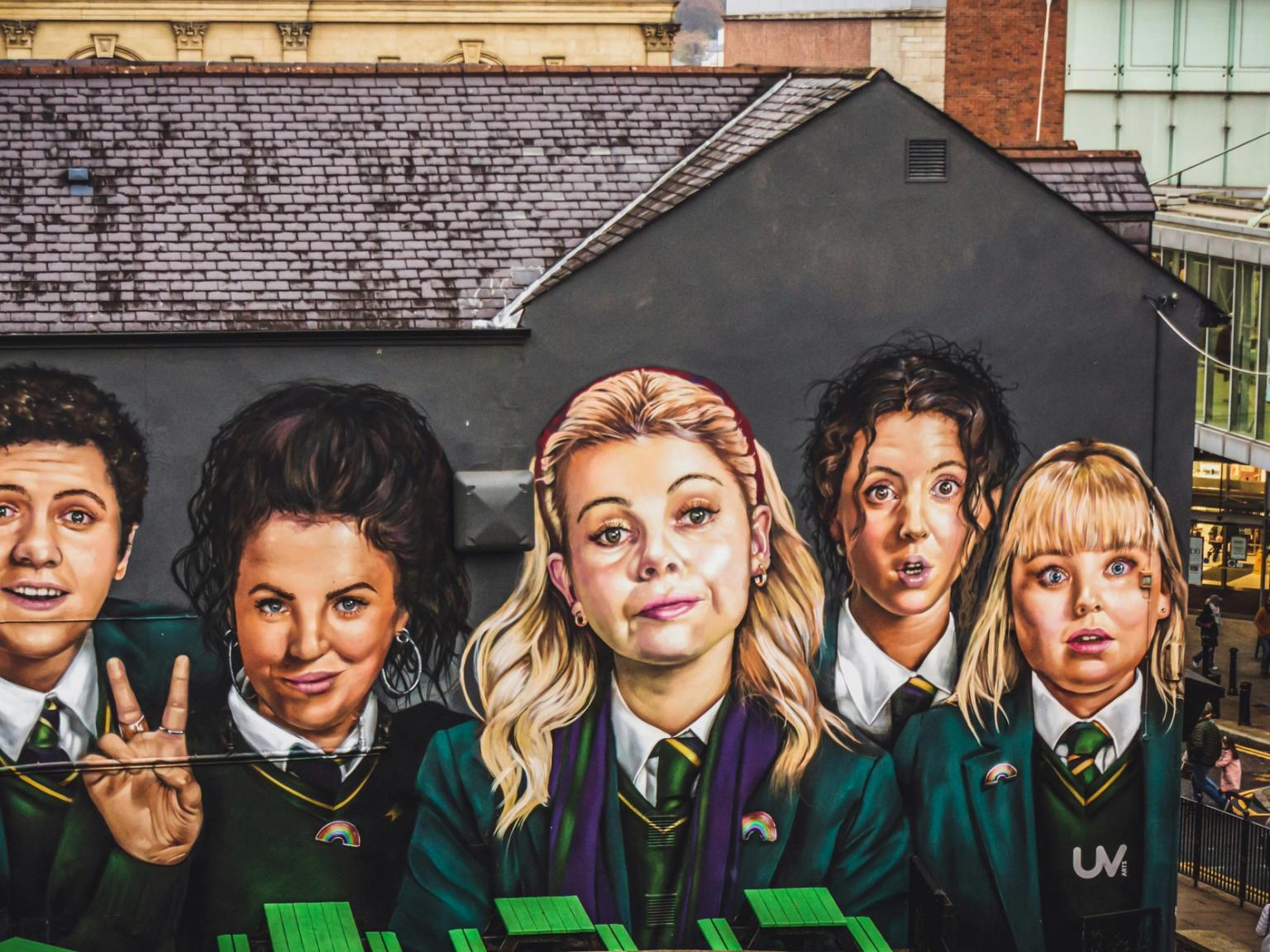 A large mural on a building depicting the five main characters from 'Derry Girls' in school uniforms.