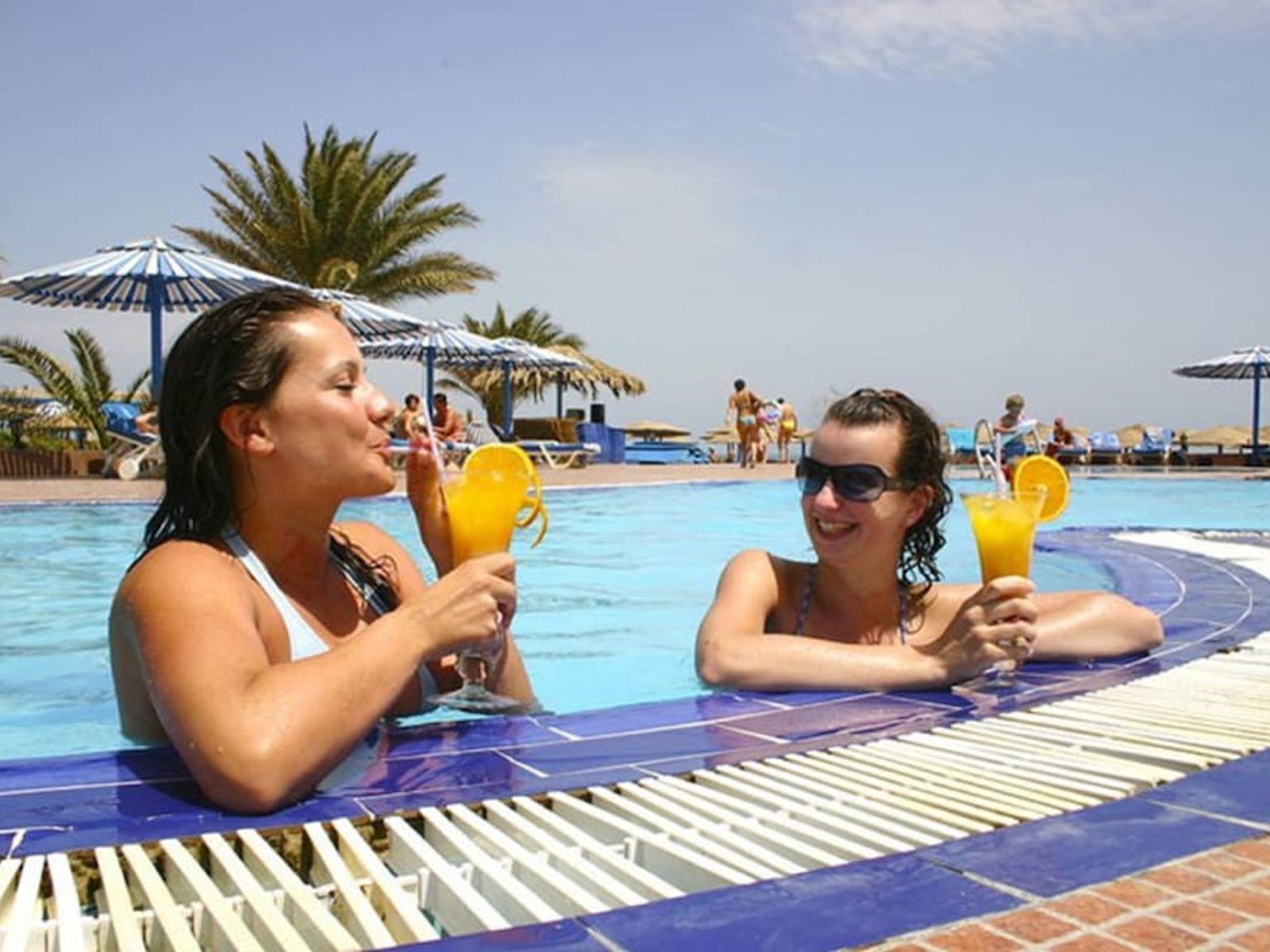 to kvinner drikker cocktails i et svømmebasseng