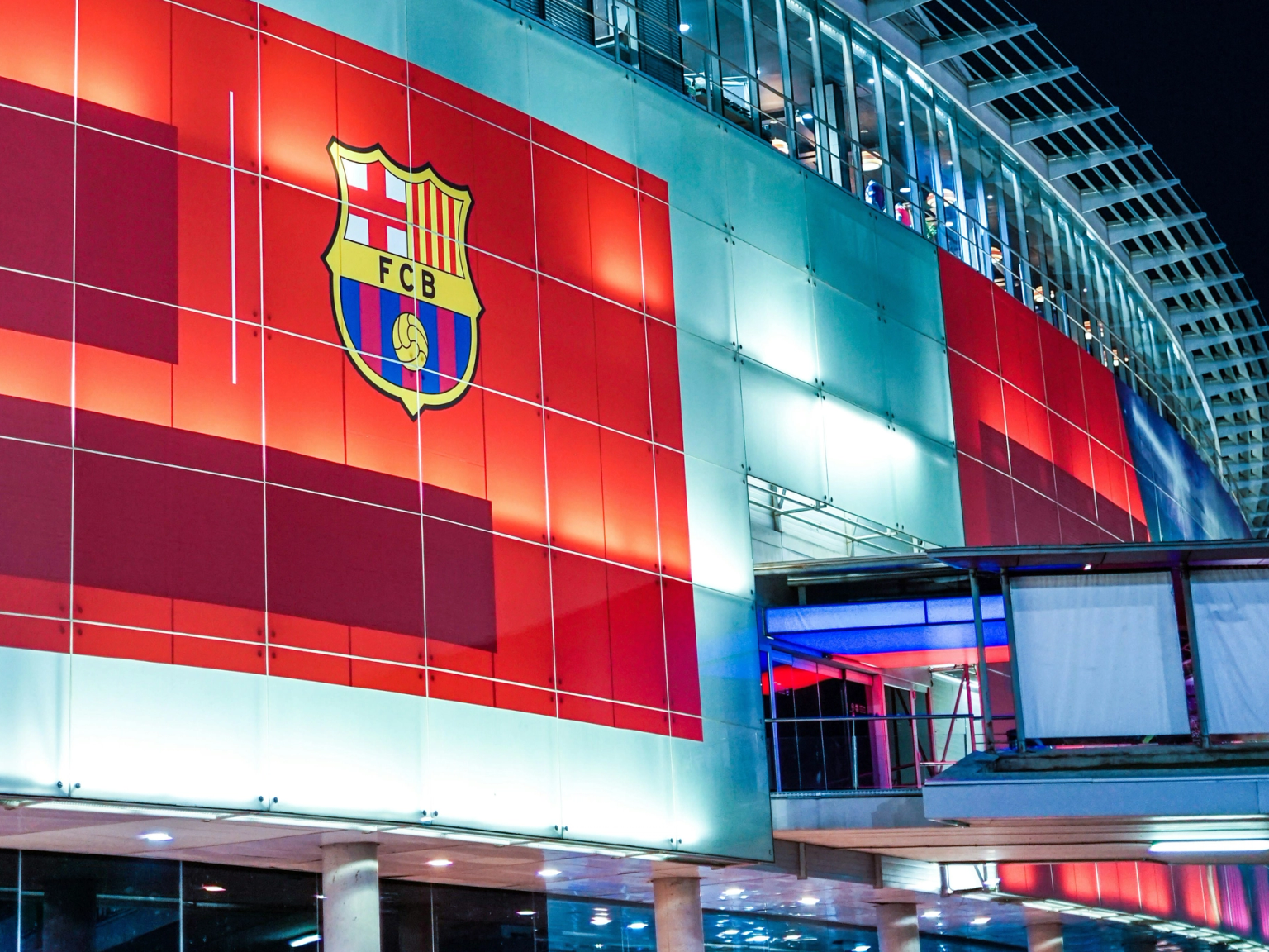 Exterior de un estadio moderno por la noche, con un gran escudo iluminado del FC Barcelona.