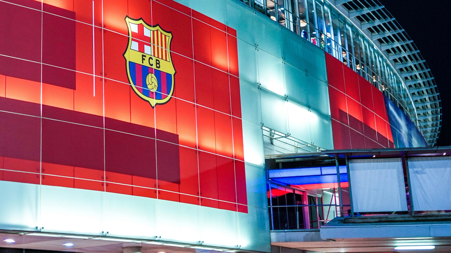Exterior of a modern stadium at night, featuring a large illuminated FC Barcelona crest.