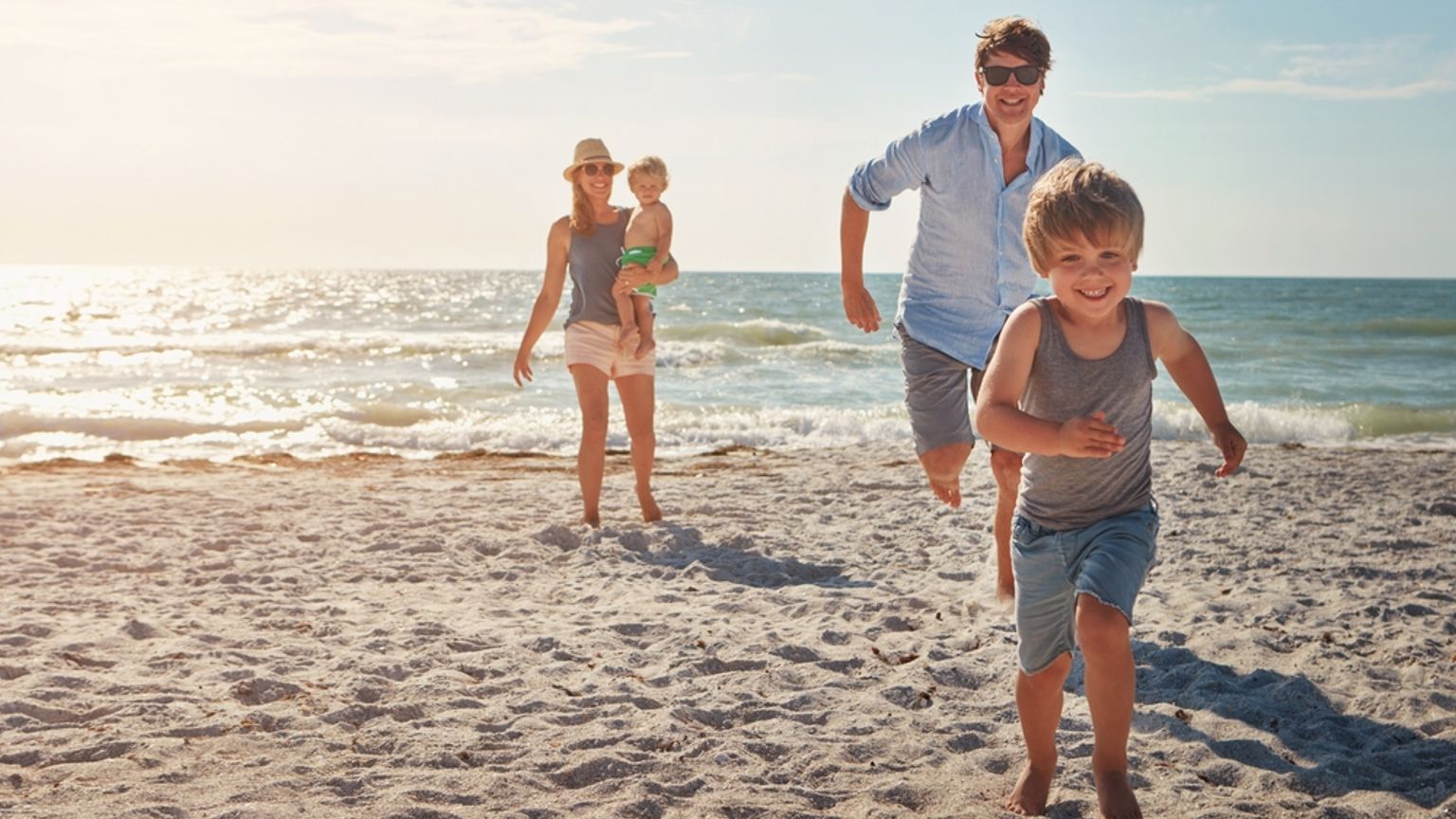 Smilende familie på fire som leker på en solrik strand.