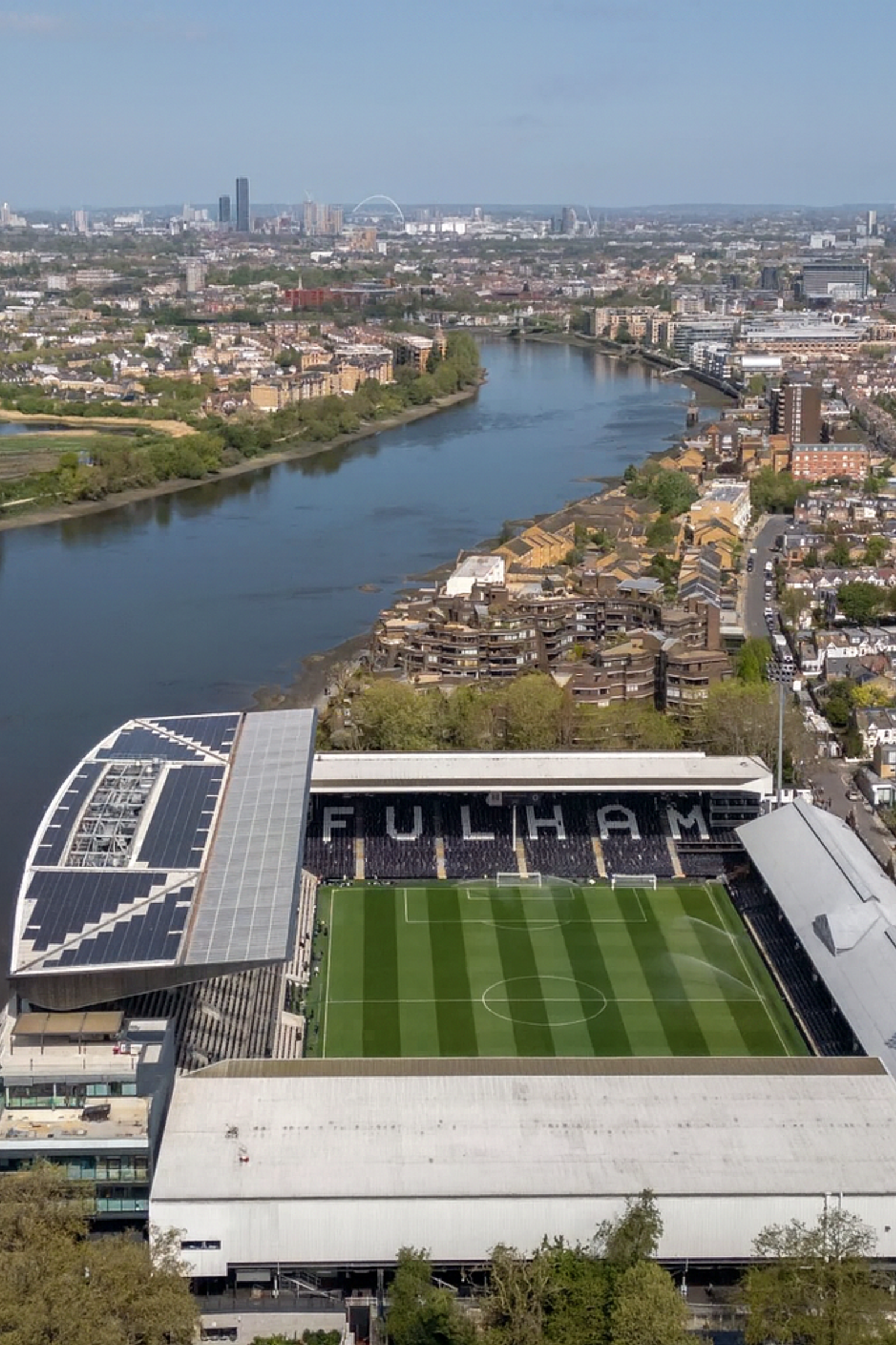 Luchtfoto van het stadion van Fulham Football Club aan de Theems, omringd door gebouwen en een verre stadsskyline.