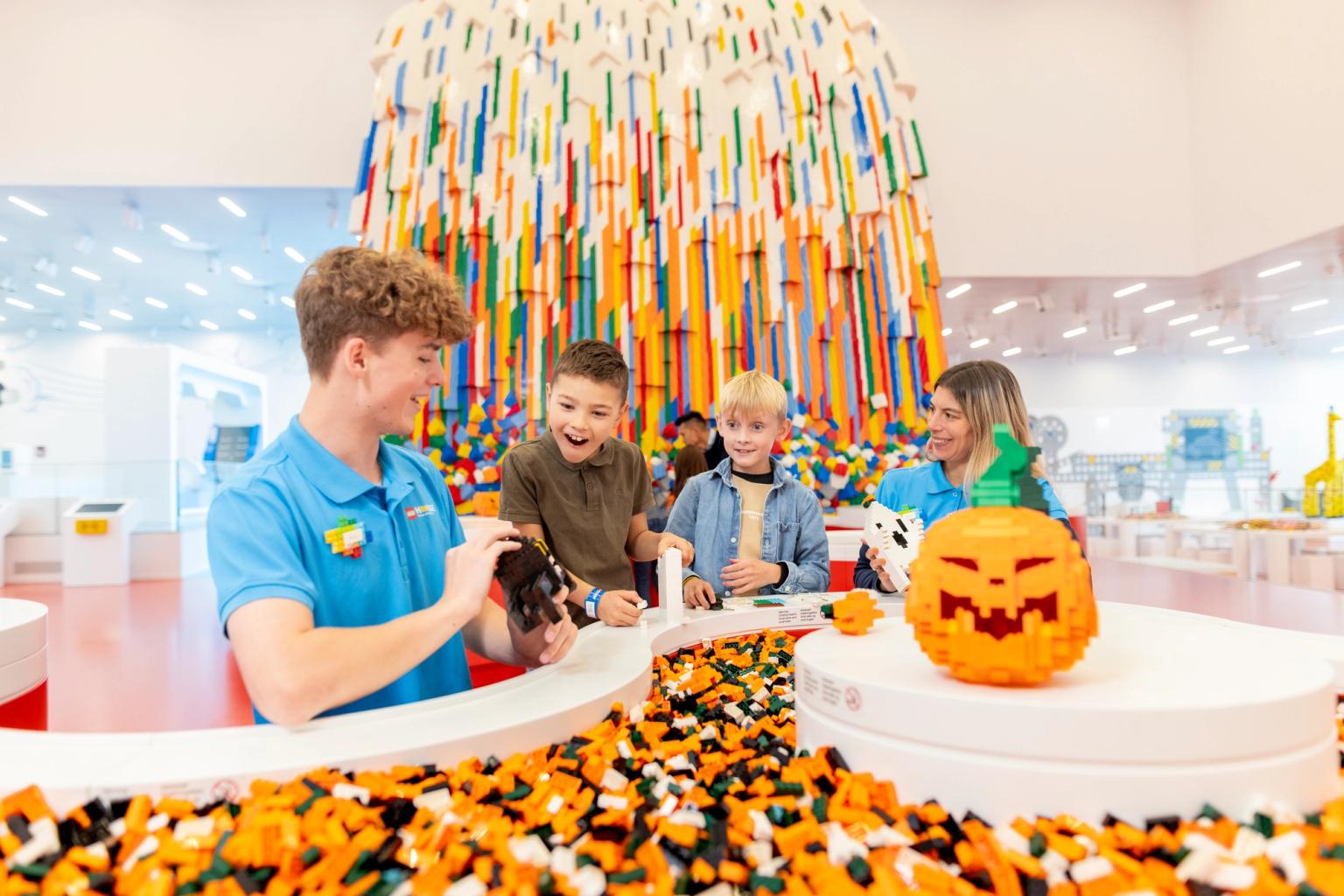 en man tar en bild av en grupp barn som leker med legobitar. Lego House, Billund