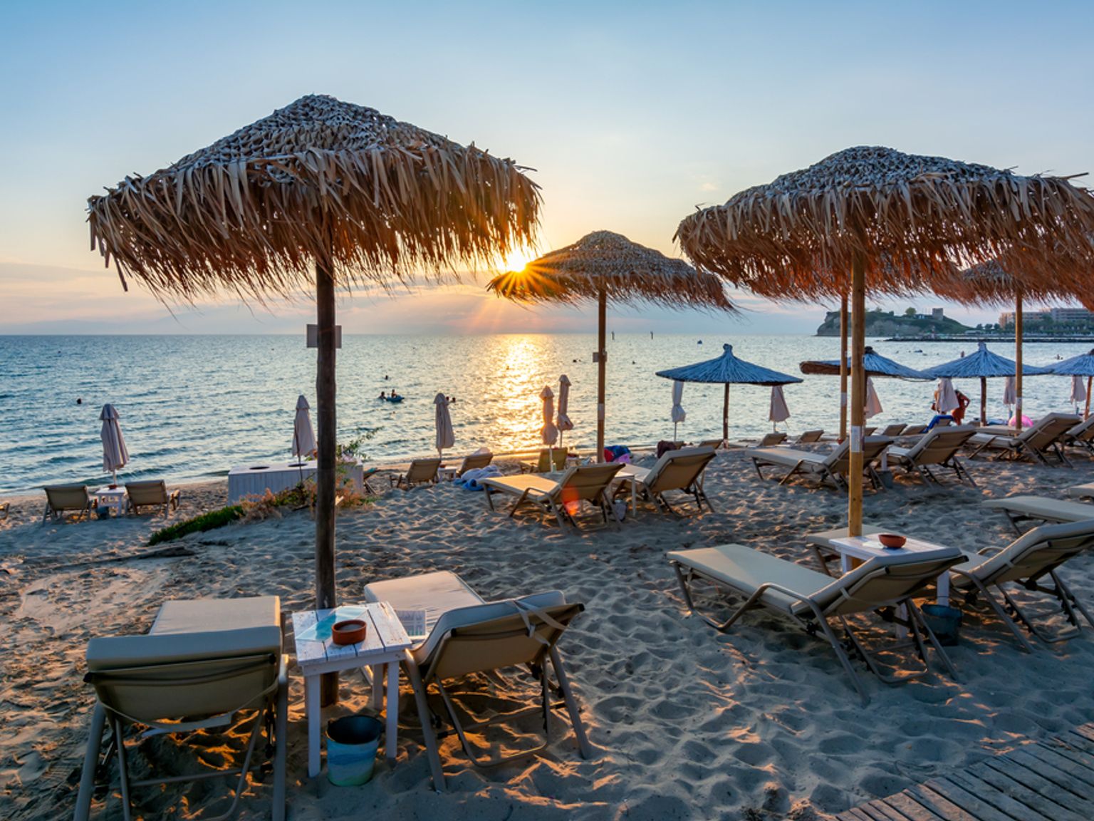 En sandstrand ved solnedgang med stråparasoller og liggestole med udsigt over havet.