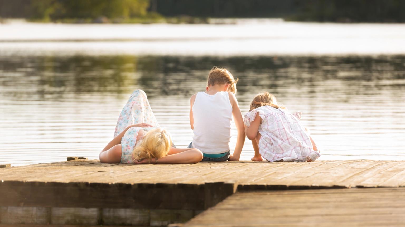 en kvinna och två barn sitter på en brygga vid en sjö