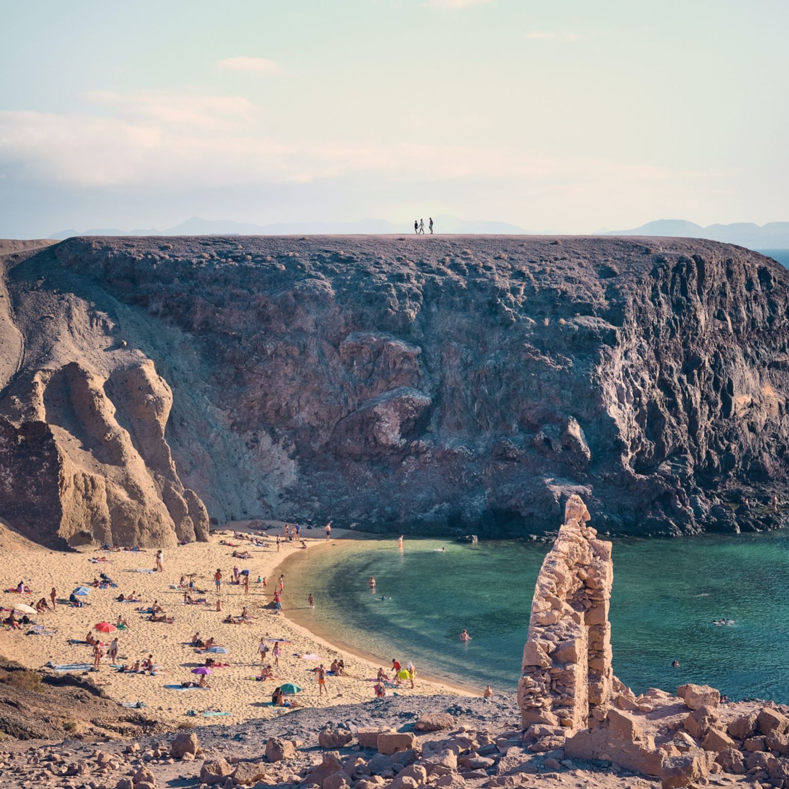 en grupp människor står på en klippig klippa med utsikt över en strand på Lanzarote.