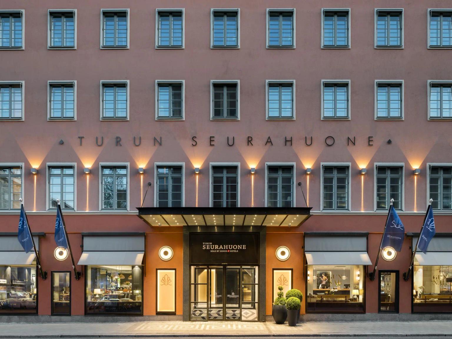 Turun Seurahuone-hotellin etunäkymä, vaaleanpunainen rakennus, jossa on valaistu sisäänkäynti ja rivi ikkunoita.