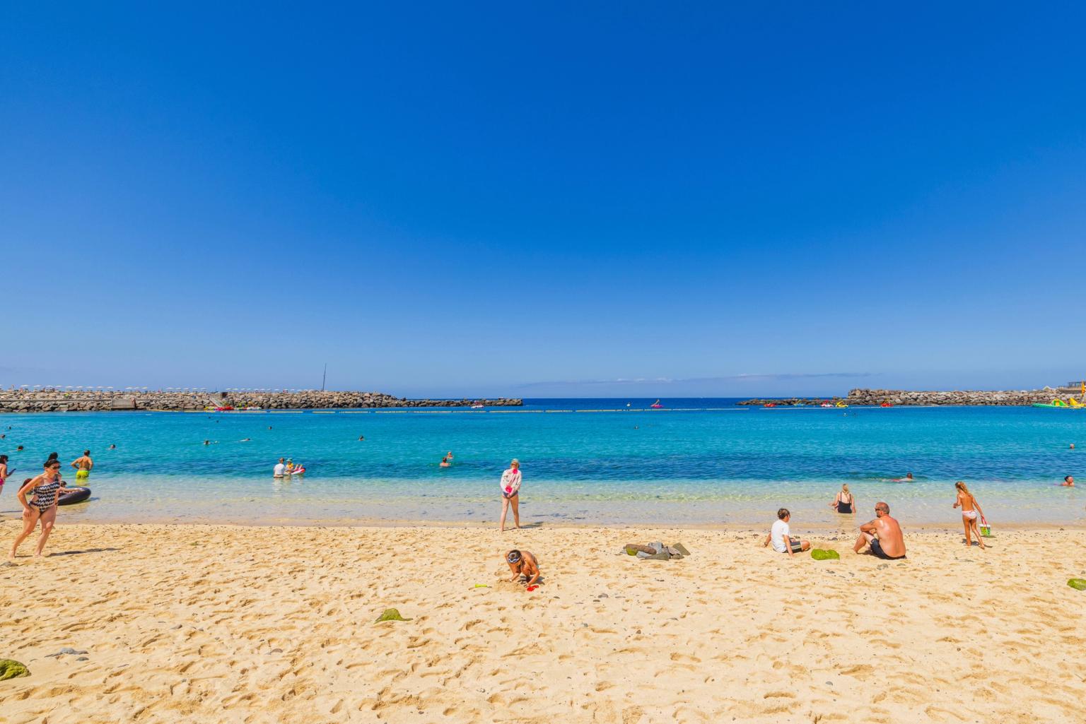 en grupp människor sitter på en sandstrand nära havet på Gran Canaria.