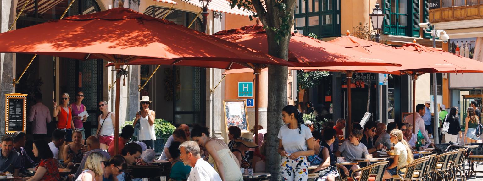 a group of people are sitting at tables under red umbrellas outside of a restaurant