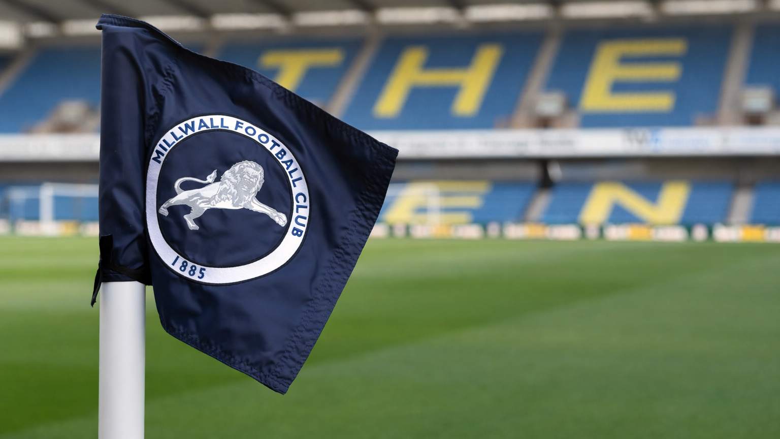 Millwall FC corner flag on a football pitch with stadium seats in the background spelling "THE DEN".
