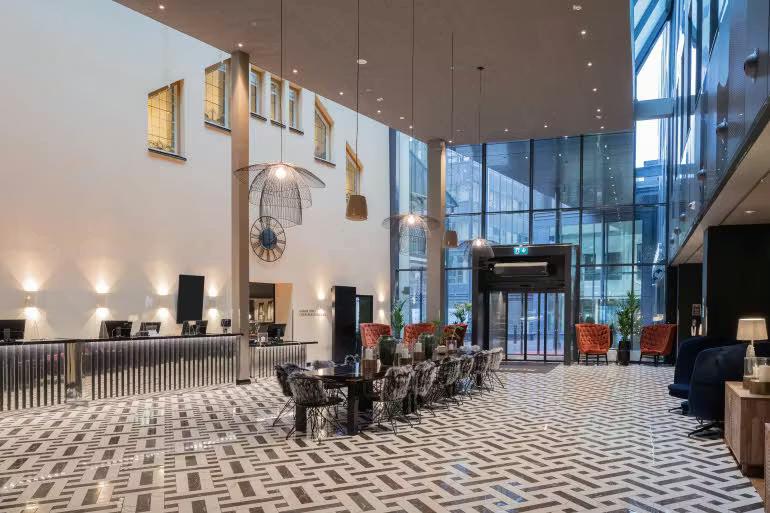 En moderne, rummelig hotellobby med en lang reception, mønstret gulv og forskellige siddeområder.